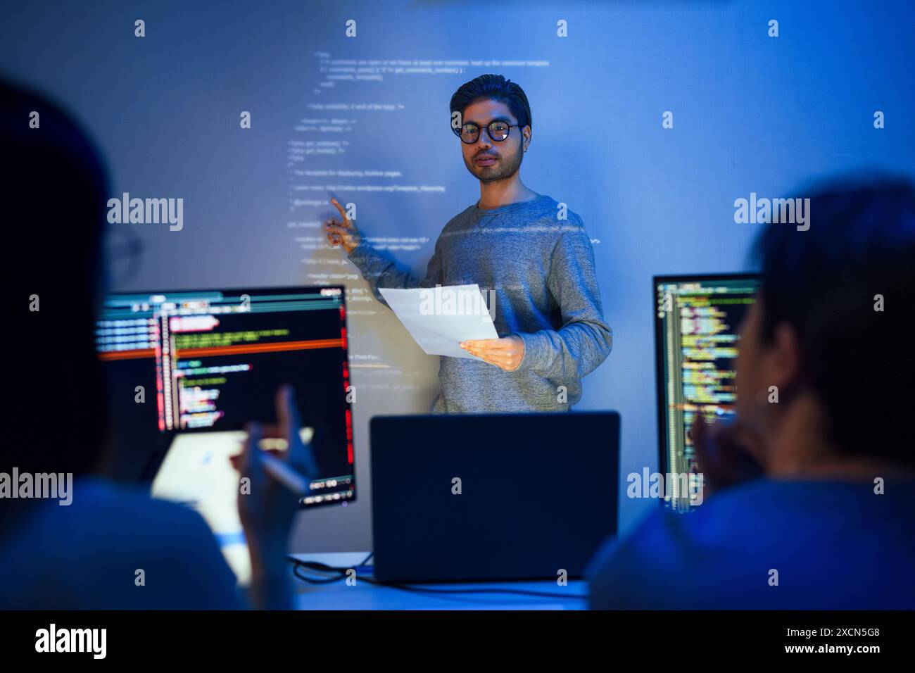 asiatische Entwickler leiten die Sitzung zur Codeüberprüfung und zeigen auf Code, der an der Wand projiziert wird, zusammen mit Kollegen, Teamarbeit und Wissensaustausch über Software Stockfoto