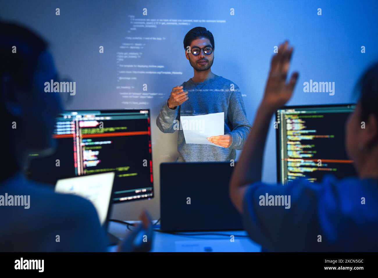 Der Entwickler führt eine Besprechung zur Codeüberprüfung durch, zeigt auf den projizierten Code an der Wand, wobei Kollegen sich beteiligen und Fragen stellen Stockfoto