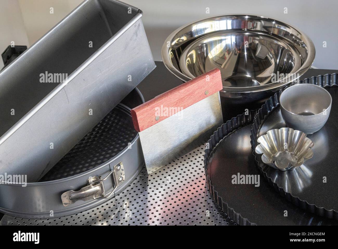 Verschiedene Küchenbackformen und -Utensilien einschließlich einer Kuchenform, Mischschalen, Teigschneider, Brotform, Mesh, Quiche-Tablett, Stockfoto