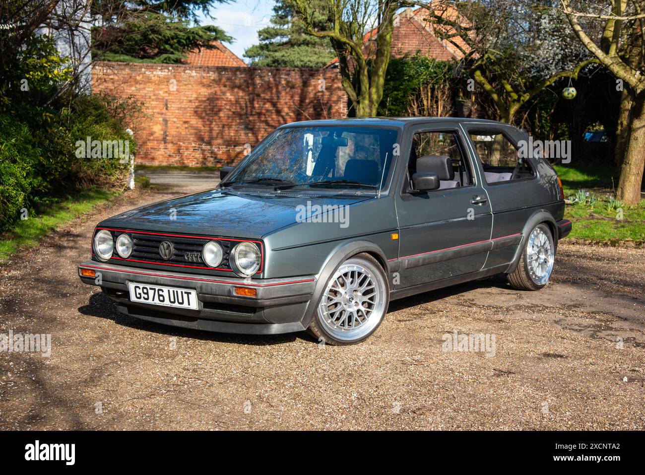 Volkswagen Golf GTi parkt auf einer Einfahrt mit Bäumen und einem Garten dahinter Stockfoto