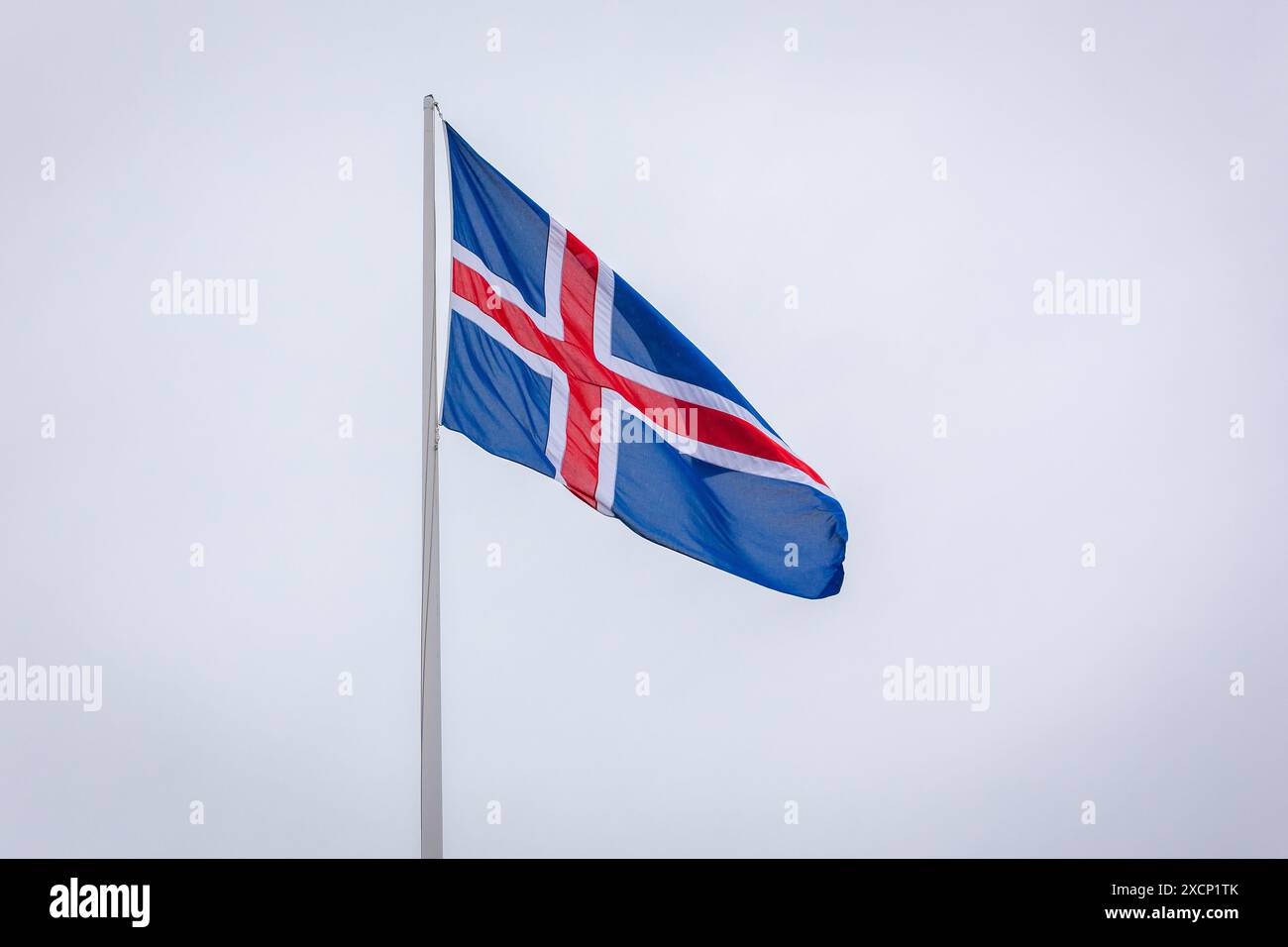 Die isländische Nationalflagge mit rotem und weißem Kreuz auf blauem Hintergrund, die im Wind vor blauem Himmel fliegt. Stockfoto
