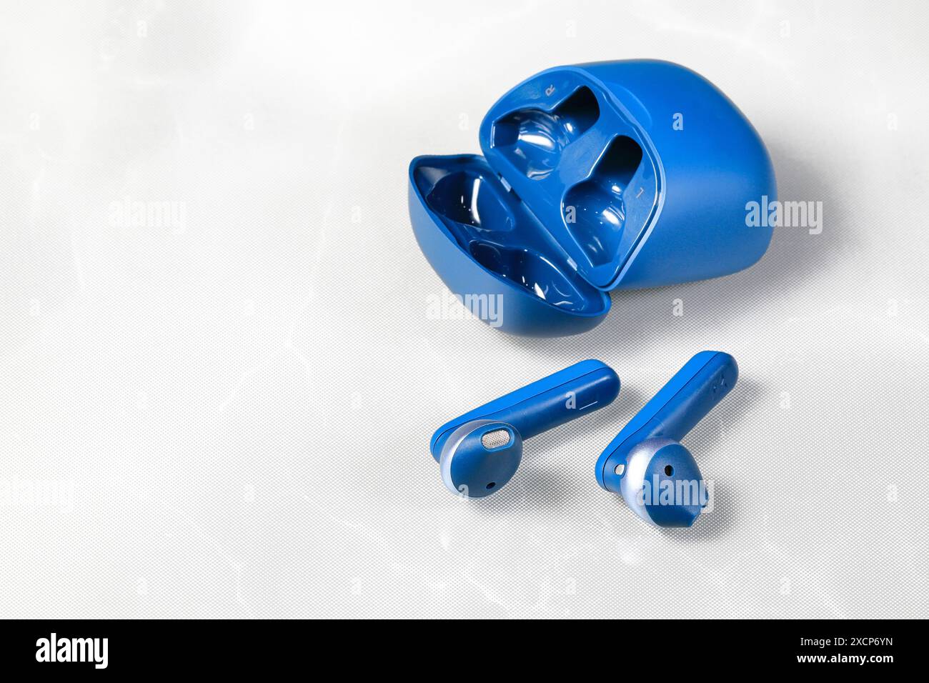 Blauer bluetooth kabelloser Kopfhörer oder Ohrhörer oder Kopfhörer mit Ladetasche auf weißem Hintergrund. Stockfoto