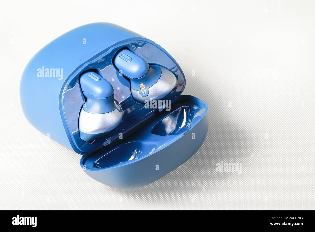 Blauer bluetooth kabelloser Kopfhörer oder Ohrhörer oder Kopfhörer mit Ladetasche auf weißem Hintergrund. Stockfoto
