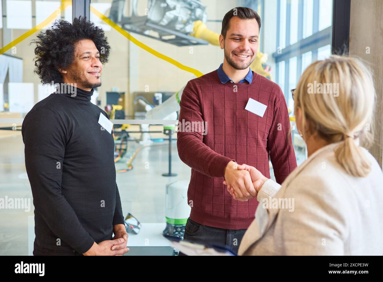 Zwei Männer begrüßen eine Frau mit einem Handschlag bei einem Robotik-Training, was auf eine professionelle und kollaborative Umgebung hindeutet. Stockfoto