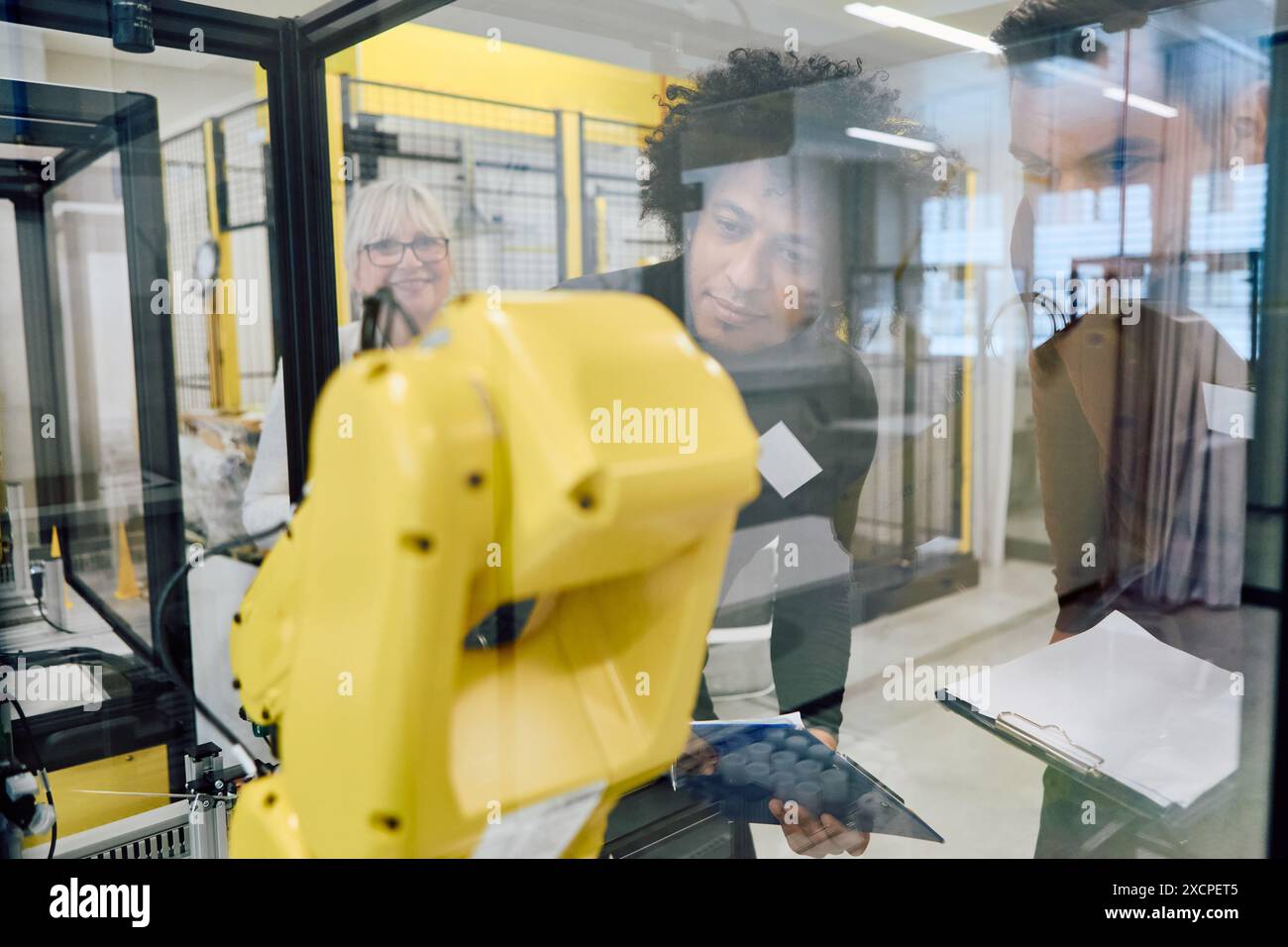 Team von Ingenieuren, die gemeinsam einen Roboterarm in einer Industrieanlage programmieren und inspizieren. Konzepte von Technologie, Teamwork und Prozess A Stockfoto