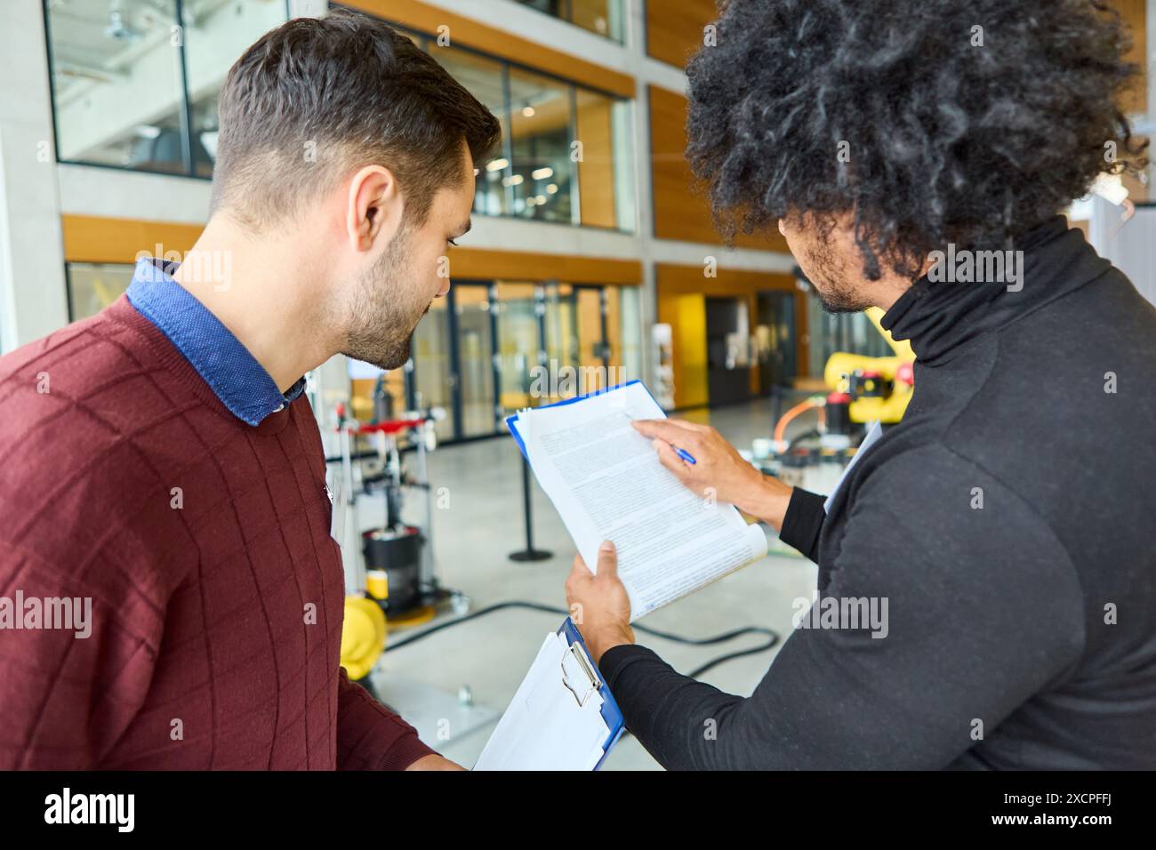 Zwei Ingenieure prüfen die Dokumentation und diskutieren Robotik- und Automatisierungslösungen in einer modernen Büroumgebung. Stockfoto