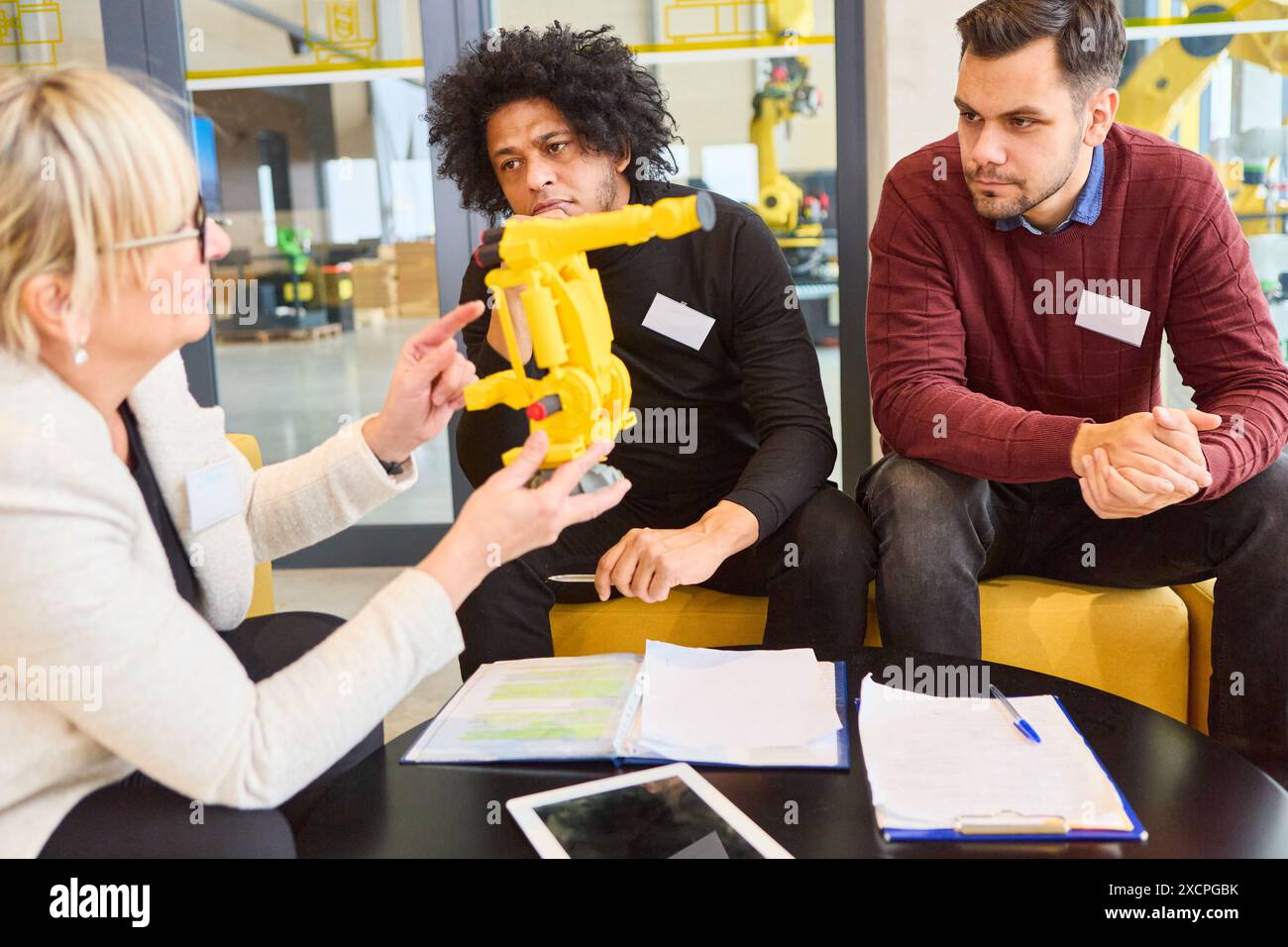 Team im Büro diskutiert Robotikentwicklung und Prozessautomatisierung unter Verwendung eines Greiferarmmodells. Ideal für Engineering, Programmierung und Industriekonzeption Stockfoto