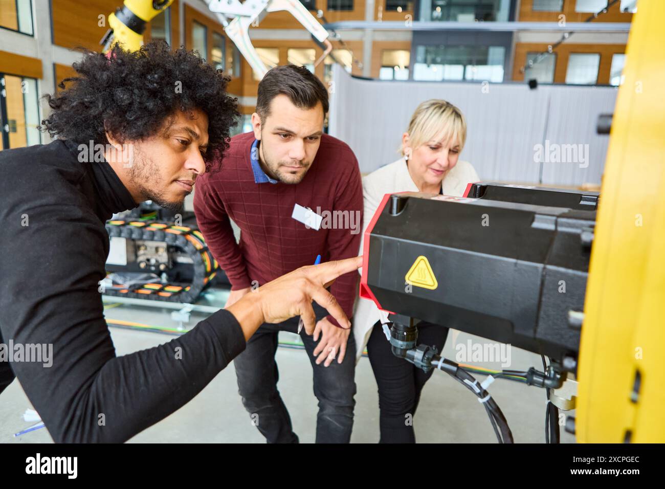 Gruppe von Ingenieuren, die gemeinsam an der Programmierung und Inspektion eines Roboterarms arbeiten und sich auf industrielle Automatisierung und technologische Fortschritte konzentrieren. Stockfoto