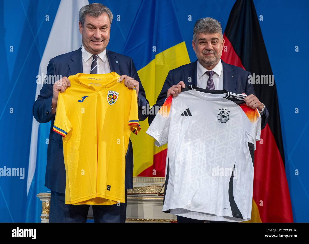 18. Juni 2024, Bayern, München: Markus Söder, (l, CSU) Ministerpräsident von Bayern, und rumänischer Premierminister Marcel Ciolacu halten sich nach einer gemeinsamen Pressekonferenz gegenseitig die Fußballtrikots vor die Kamera. Das bayerische und das rumänische Kabinett hatten sich zuvor in der bayerischen Hauptstadt zusammengefunden. Foto: Peter Kneffel/dpa Stockfoto