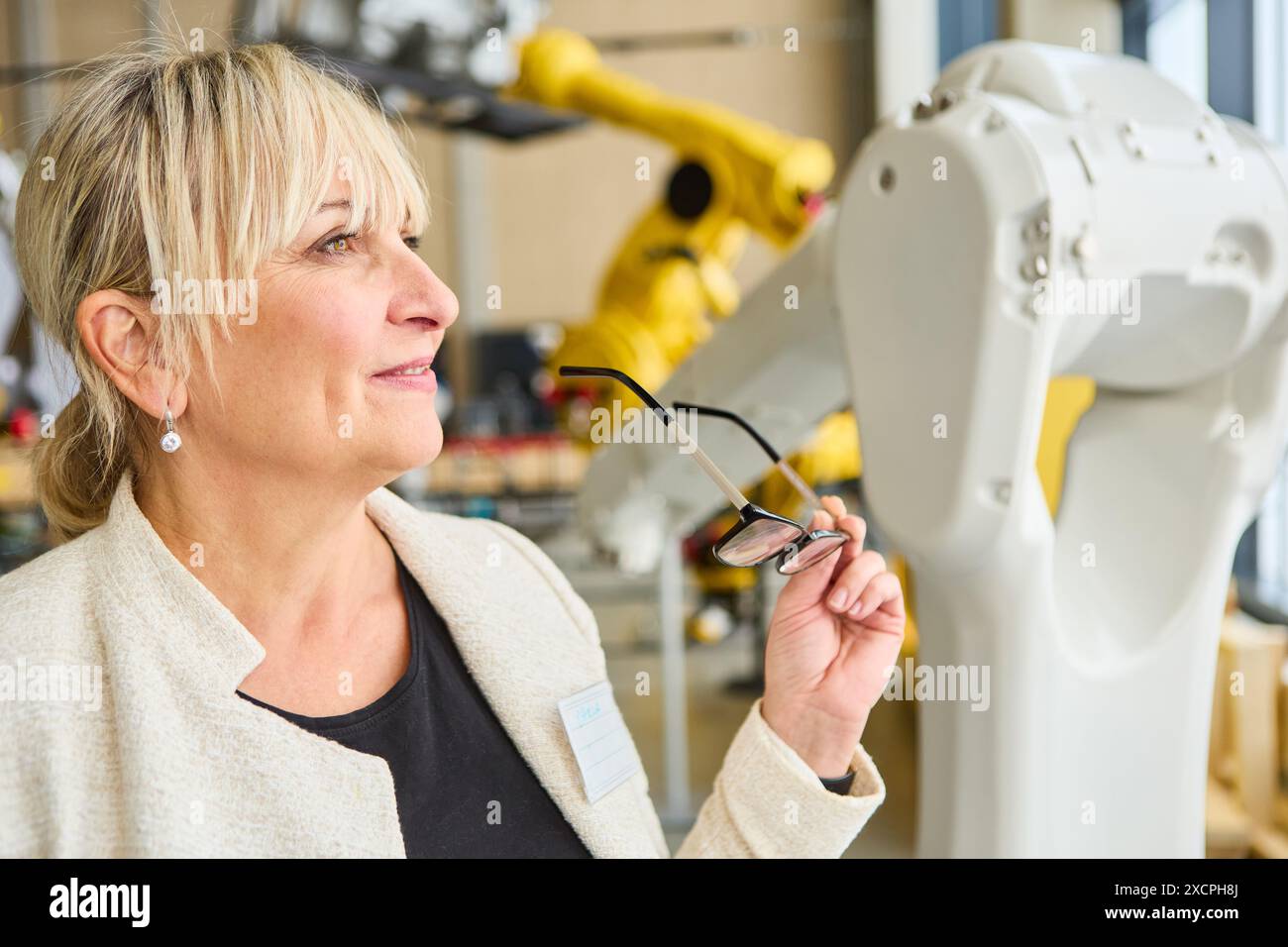 Leitende Ingenieurin beobachtet einen Roboterarm in einer industriellen Umgebung und zeigt technologische, automatisierte und technische Fortschritte an. Stockfoto