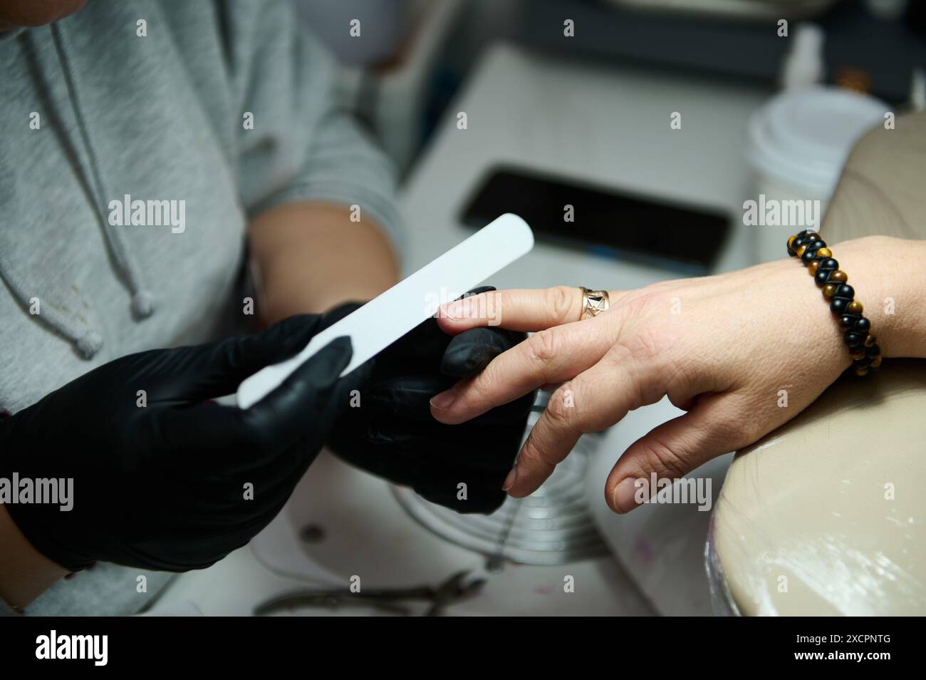Nahaufnahme eines Manikürs, der Nägel in einem Schönheitssalon feilt. Konzentrieren Sie sich auf Hände, schwarze Handschuhe und Nagelfeile. Professioneller Manikürservice. Stockfoto