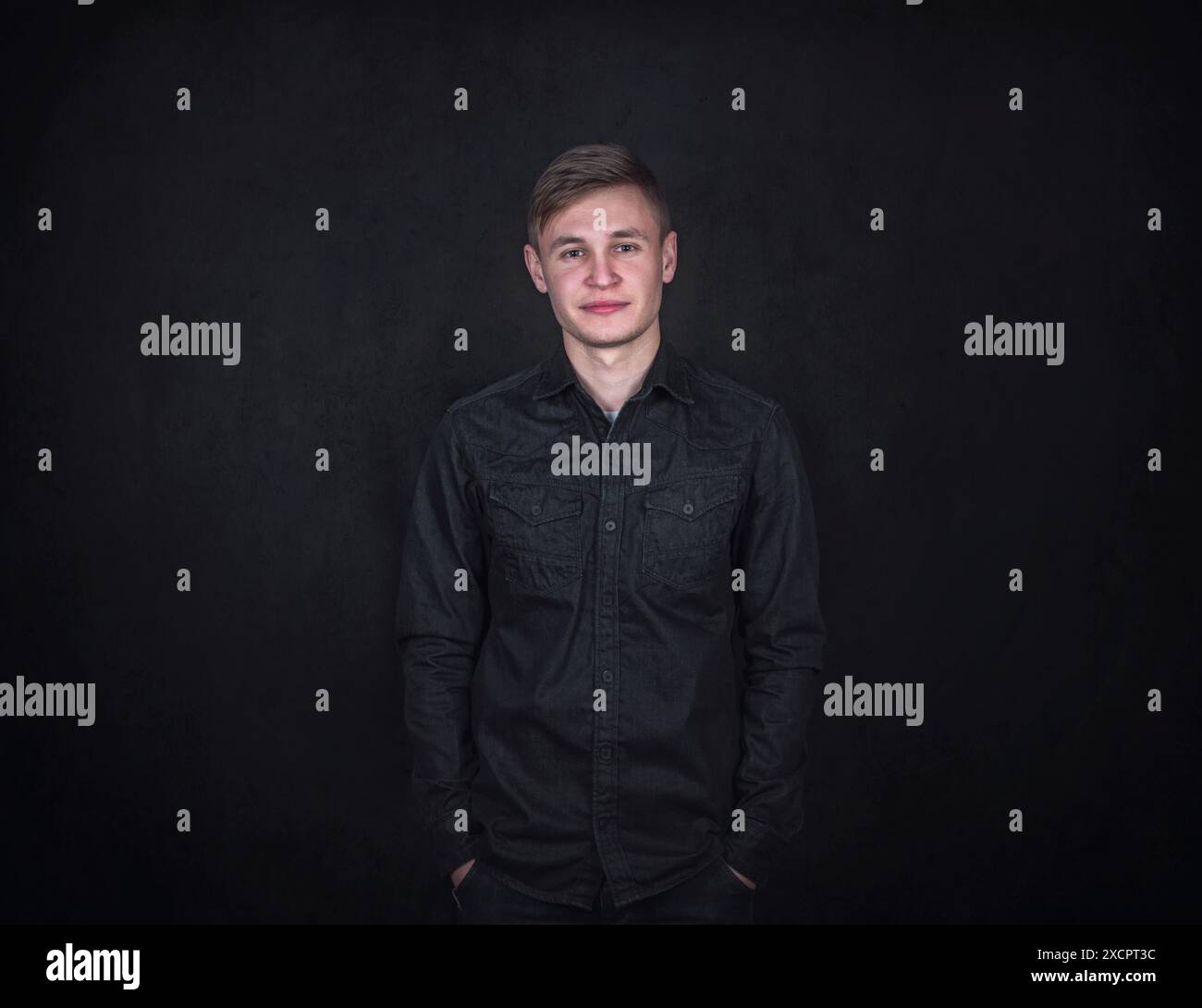Selbstbewusstes und entspanntes Porträt junger Männer, die Hände in den Taschen vor schwarzem Hintergrund halten. Unbeschwerter männlicher Student mit positivem Gesichtsausdruck Stockfoto