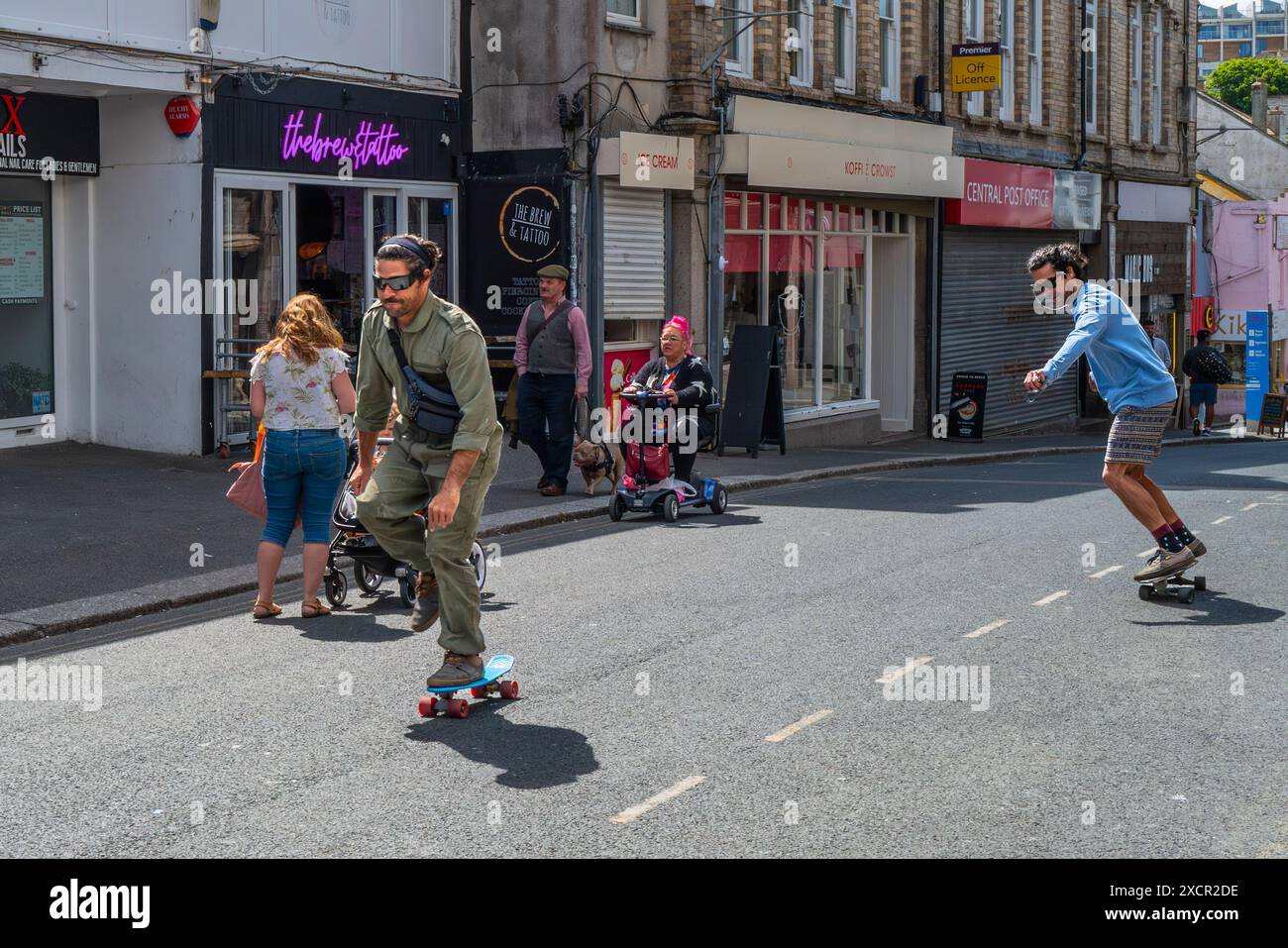 Zwei Personen, die auf einer Straße im Stadtzentrum von Newquay in Cornwall in Großbritannien Skateboarden. Stockfoto