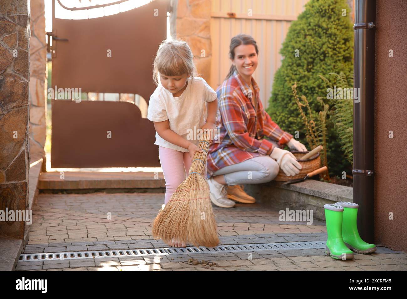 Mutter und ihre süße Tochter putzen zusammen in der Nähe des Hauses am Frühlingstag Stockfoto