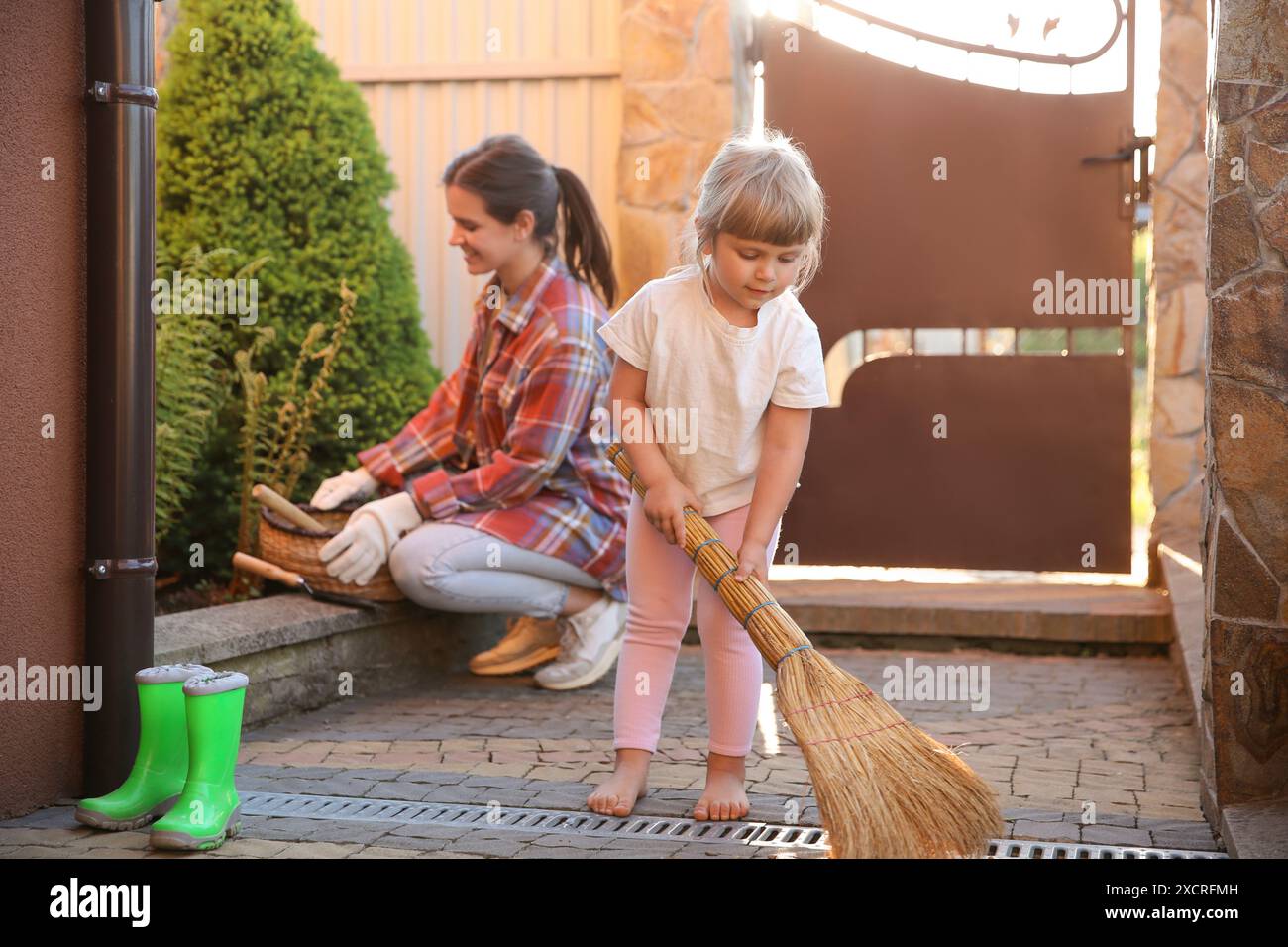 Mutter und ihre süße Tochter putzen zusammen in der Nähe des Hauses am Frühlingstag Stockfoto