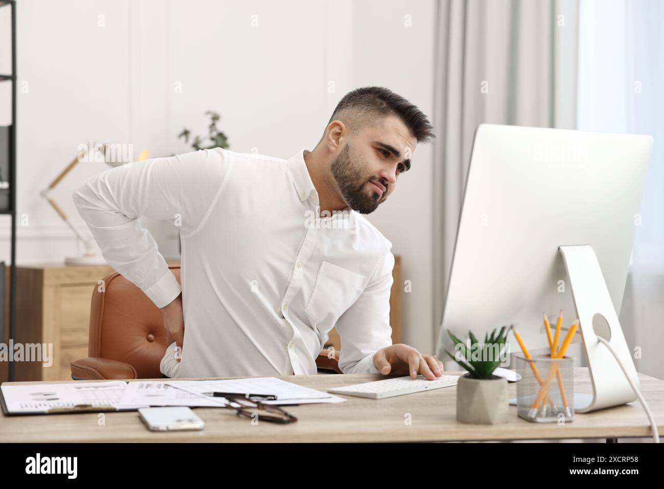 Mann mit Rückenschmerzen im Büro. Symptom einer schlechten Körperhaltung Stockfoto