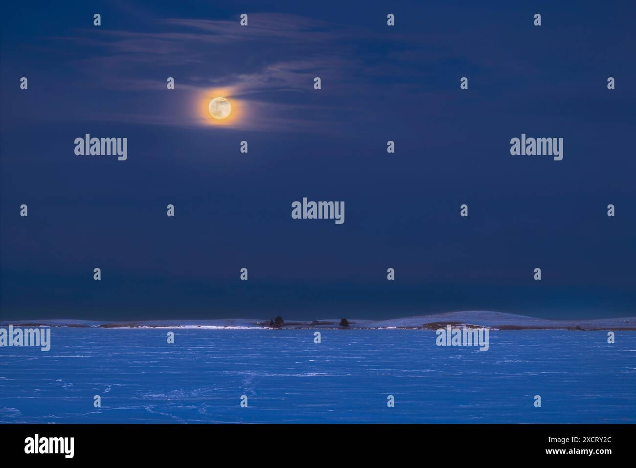 Der Aufgang des Wintermondes „Wolf“, des Vollmondes des Januar, über dem gefrorenen Stausee im Süden Albertas, 25. Januar 2024. Während Stockfoto
