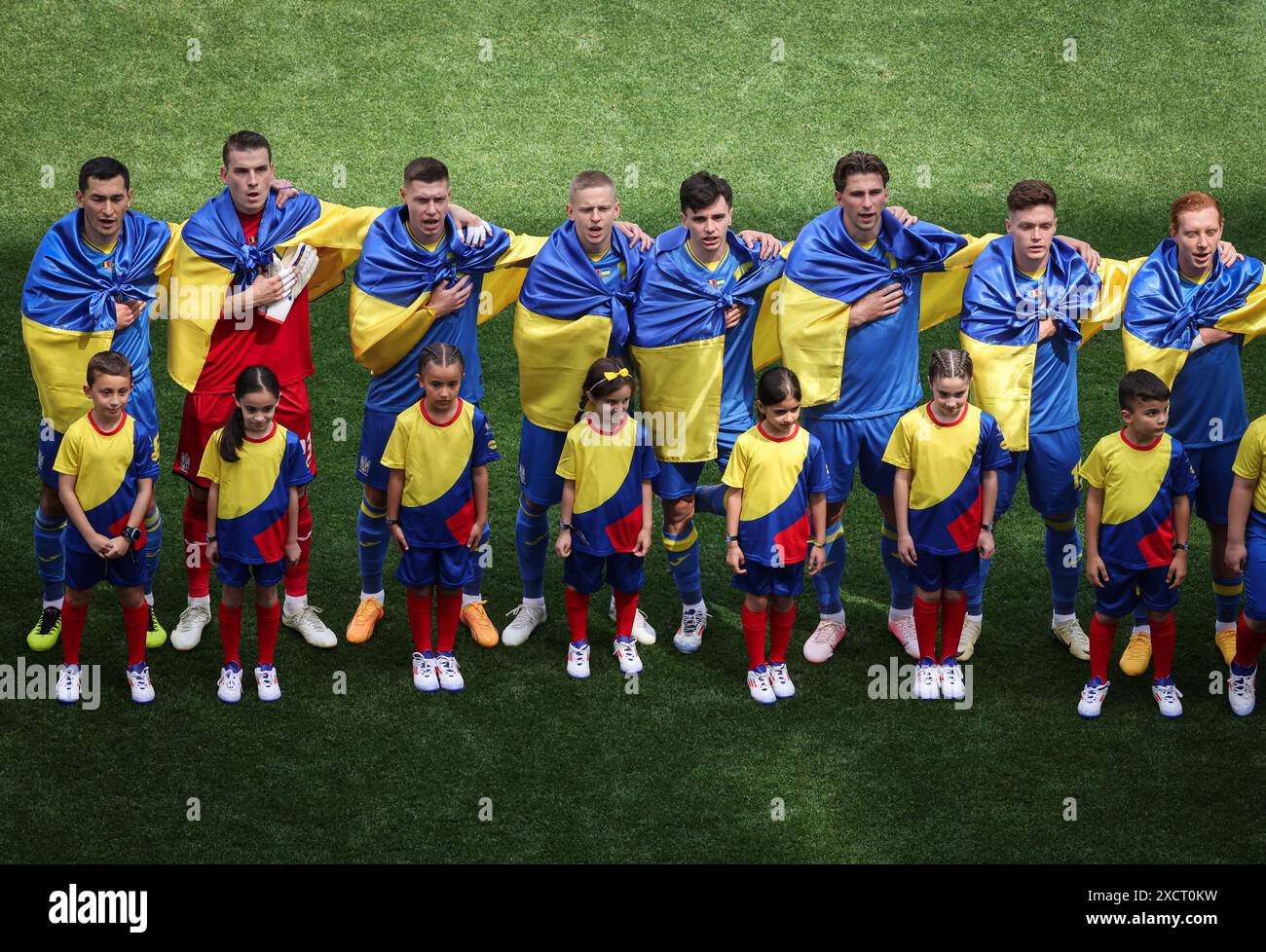 MÜNCHEN, DEUTSCHLAND - 17. JUNI: Oleksandr Zinchenko aus der Ukraine singt ihre Nationalhymne mit Teamkollegen, die die Nationalflagge der Ukraine tragen, vor dem Gruppenspiel der UEFA EURO 2024 zwischen Rumänien und der Ukraine am 17. Juni 2024 in München. © diebilderwelt / Alamy Stock Stockfoto