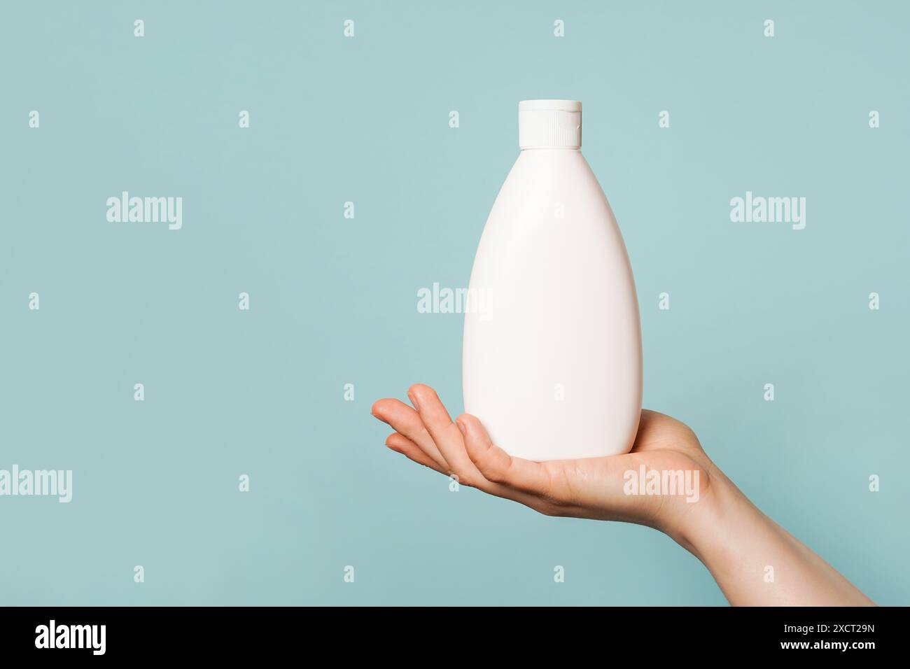 Eine Hand, die eine weiße Plastikflasche vor einem hellblauen Hintergrund hält Stockfoto