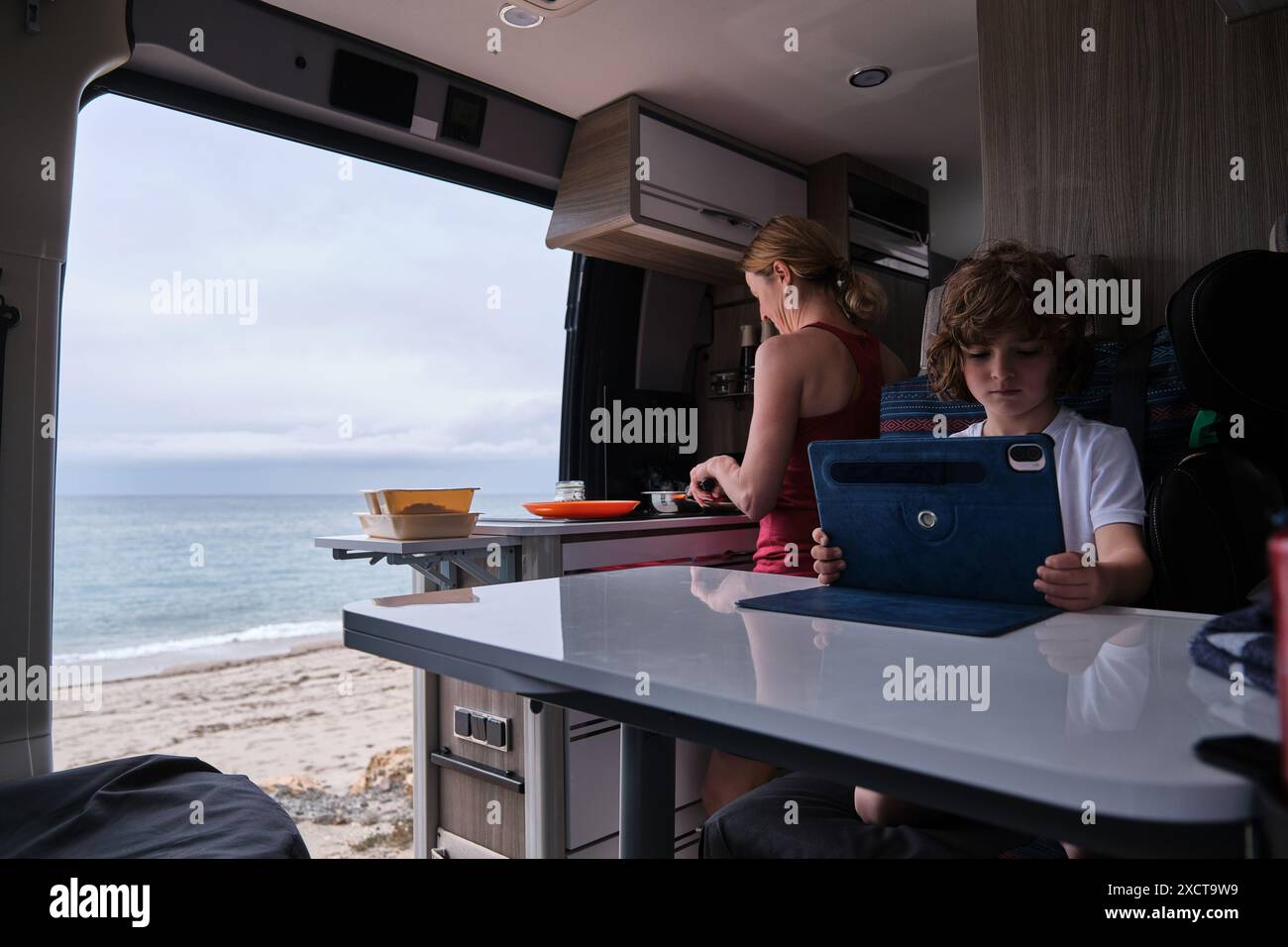 Eine Mutter kocht im Wohnmobil, während der Sohn mit einem digitalen Tablet spielt Stockfoto