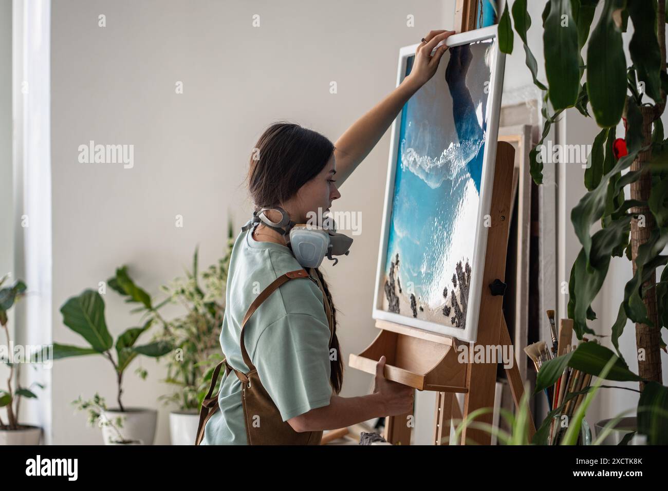 Fokussierte künstlerische Frau, die Leinwand mit Epoxidharzmalerei in flüssiger Kunsttechnik auf die Staffelei legt. Stockfoto