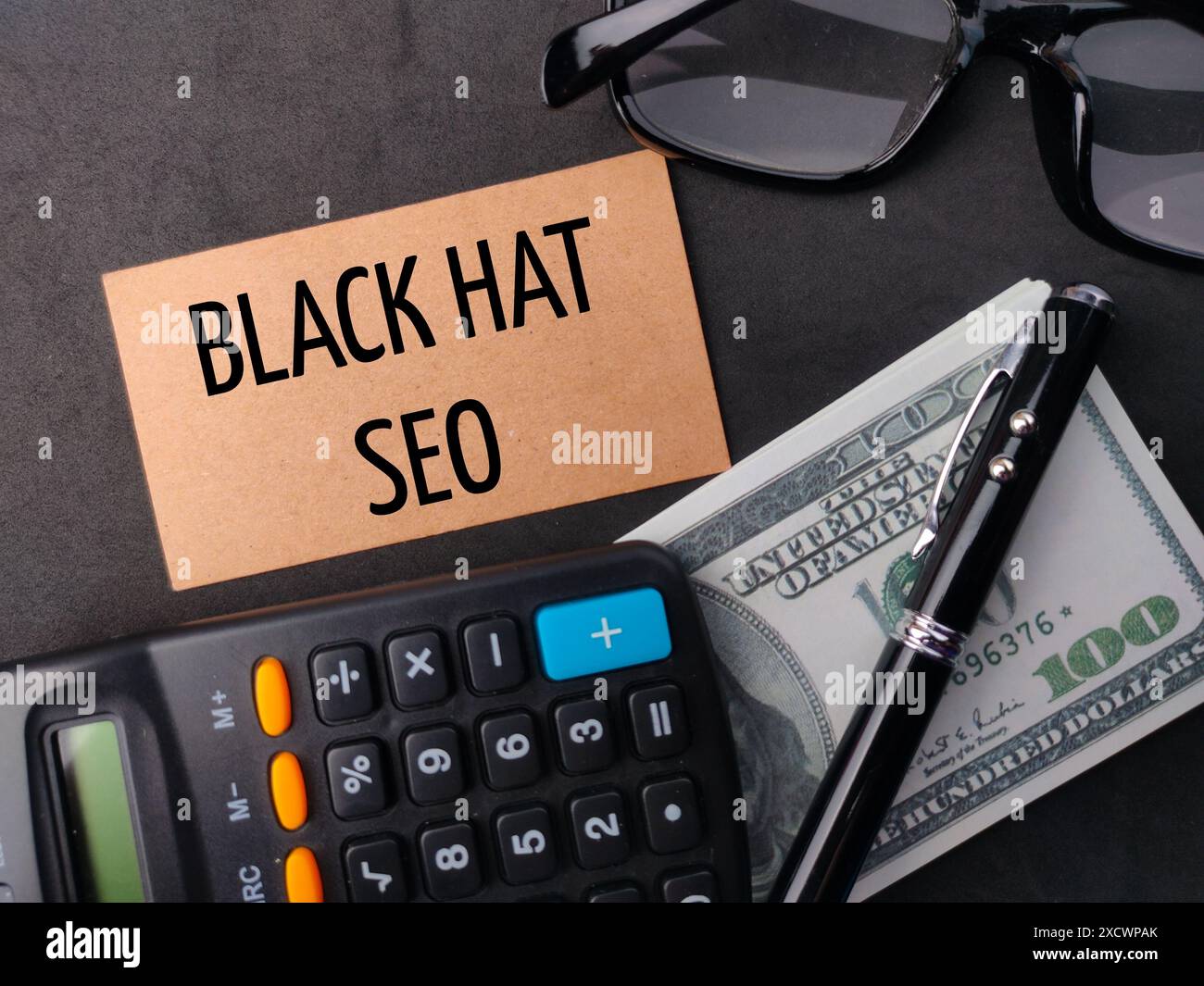 Taschenrechner, Stift, Banknoten und Brille mit SCHWARZEM HUT SEO auf schwarzem Hintergrund. Stockfoto