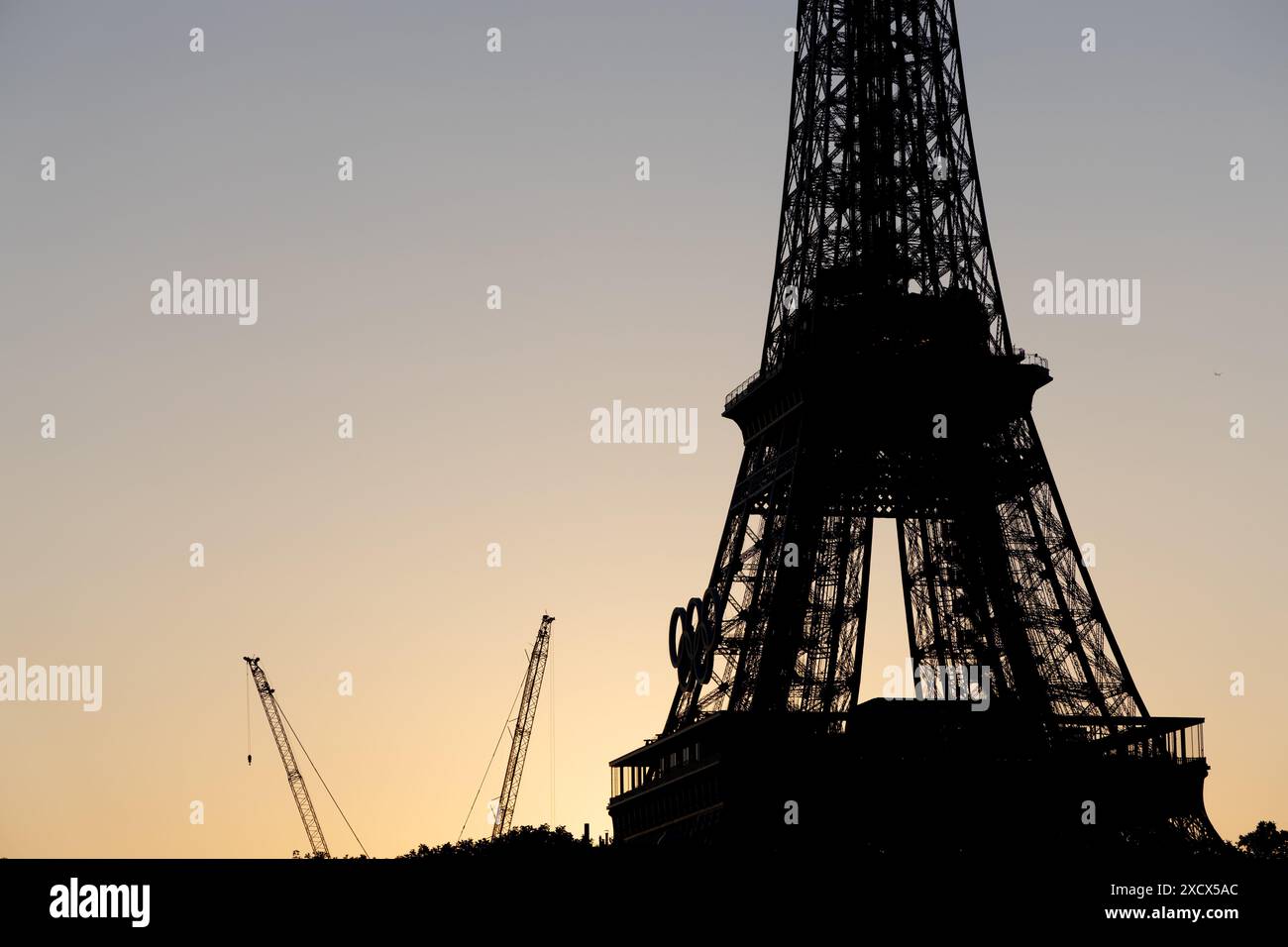 Paris, Frankreich - 07. Juni 2024: Silhouette des Eiffelturms im frühen Morgenlicht. Logo der Olympischen Spiele auf dem Turm und Baukran auf dem Boden. Stockfoto