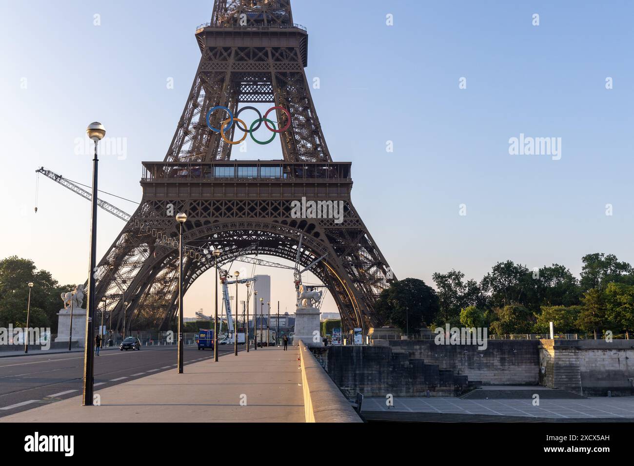 Paris, Frankreich - 07. Juni 2024: Eiffelturm im frühen Morgenlicht. Logo der Olympischen Spiele auf dem Turm und Baukran auf dem Boden. Sichtbare Personen Stockfoto