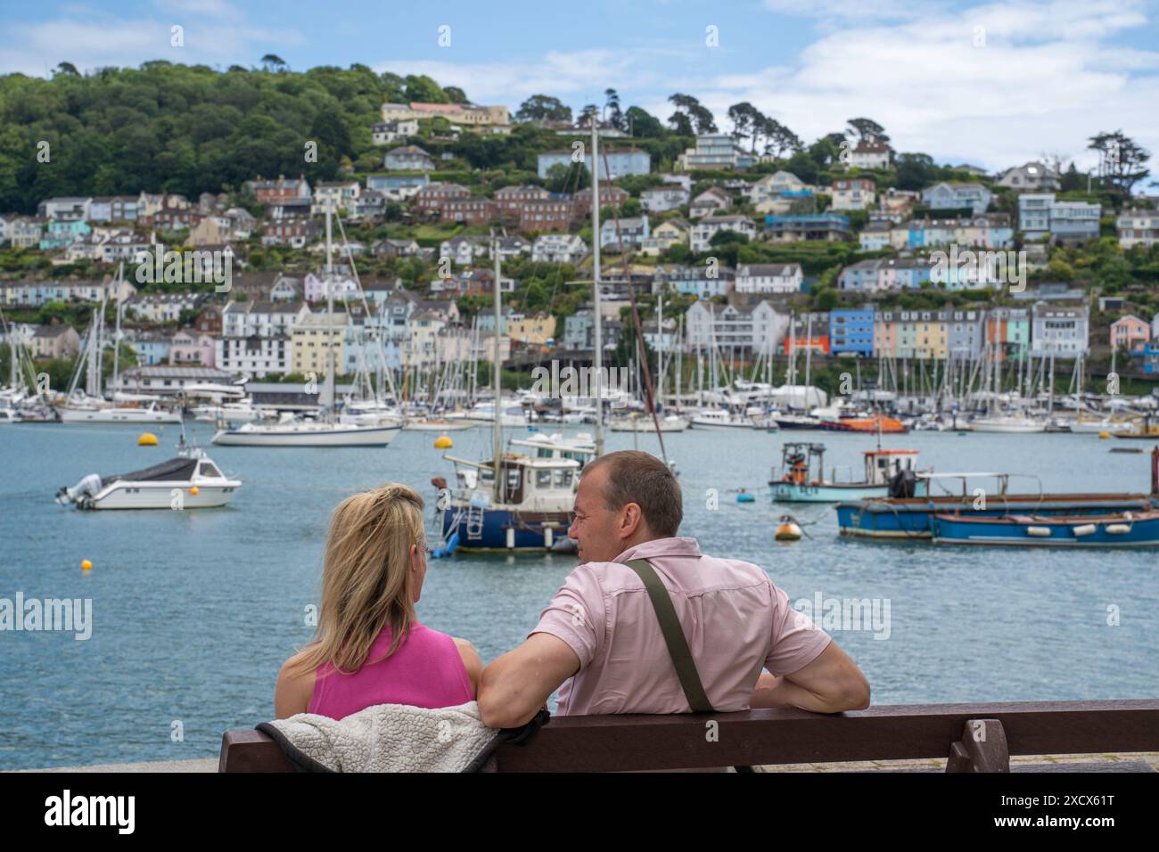 Ein Paar sitzt auf einer Bank in Dartmouth und blickt über den Fluss Dart in Richtung Kingswear. Stockfoto