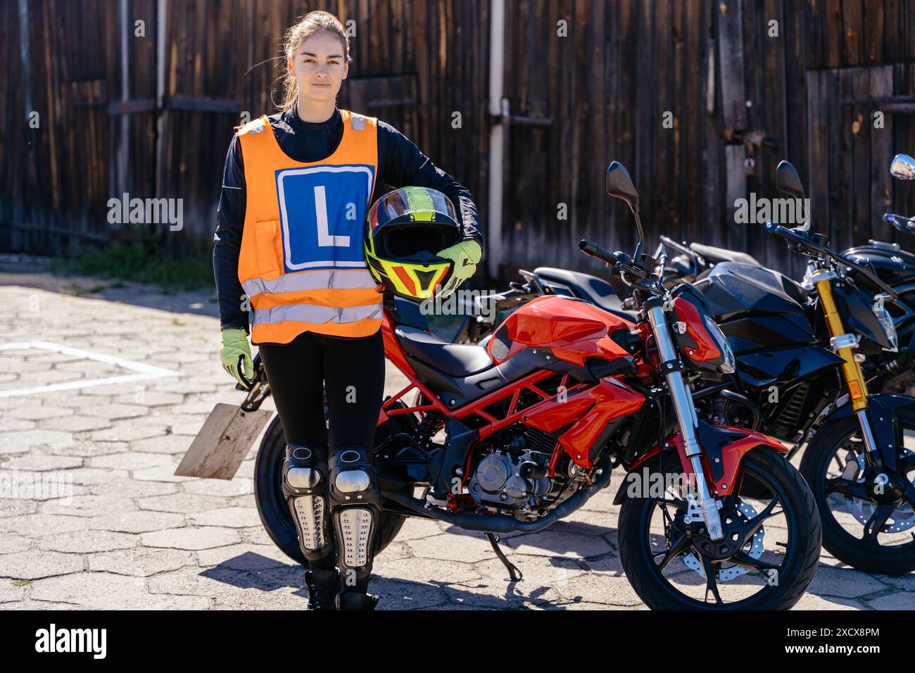 Frau in orangefarbener Weste mit mir neben rotem Motorrad Stockfoto
