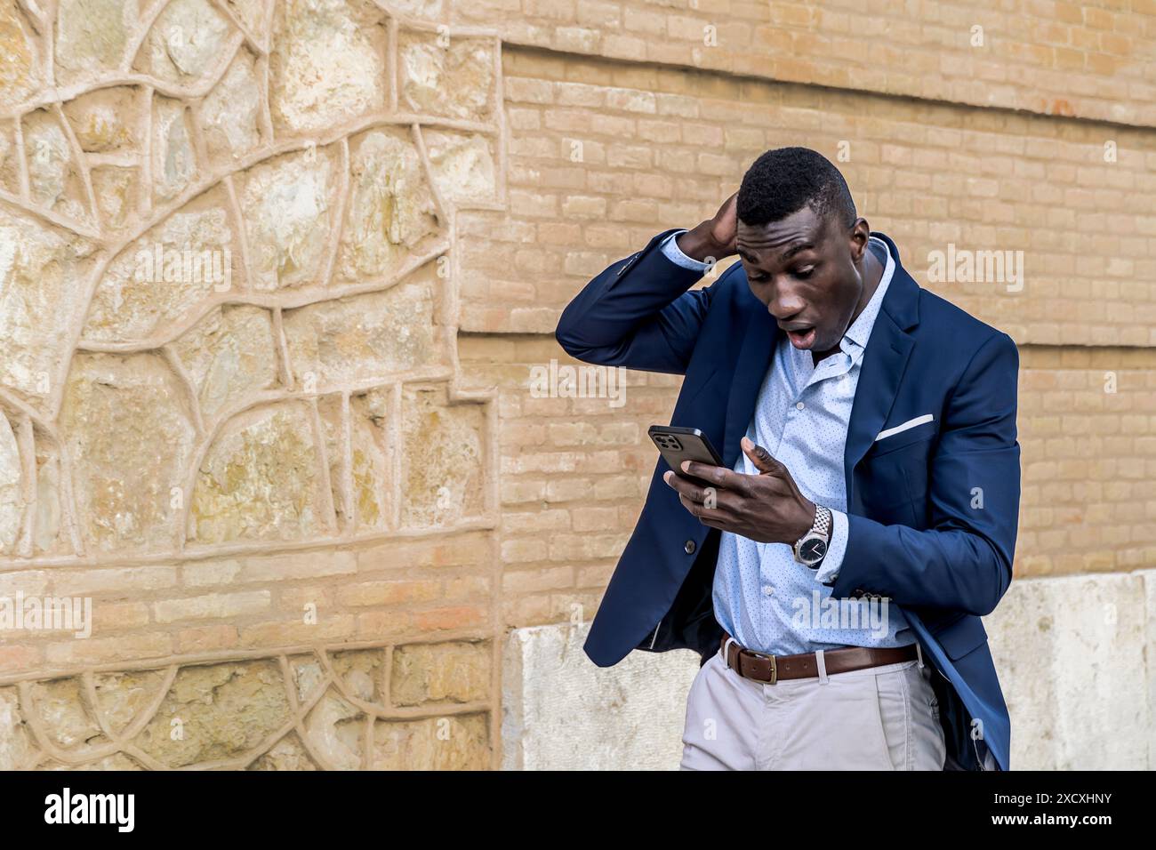 Überraschter afroamerikanischer Geschäftsmann im eleganten Anzug mit Smartphone. Schockierter Gesichtsausdruck und Technologiekonzept in der Wirtschaft. Stockfoto