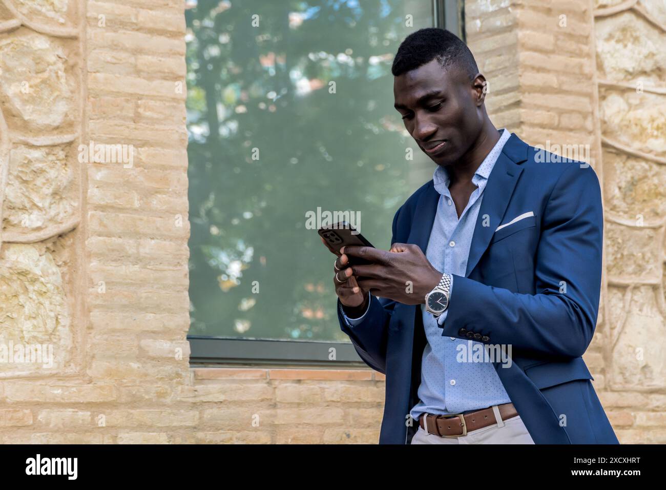 Afroamerikanischer Geschäftsmann in elegantem Anzug mit Handy. Junge Profis lächeln und gehen, mit Platz für Text im Bild. Geschäftlich Stockfoto