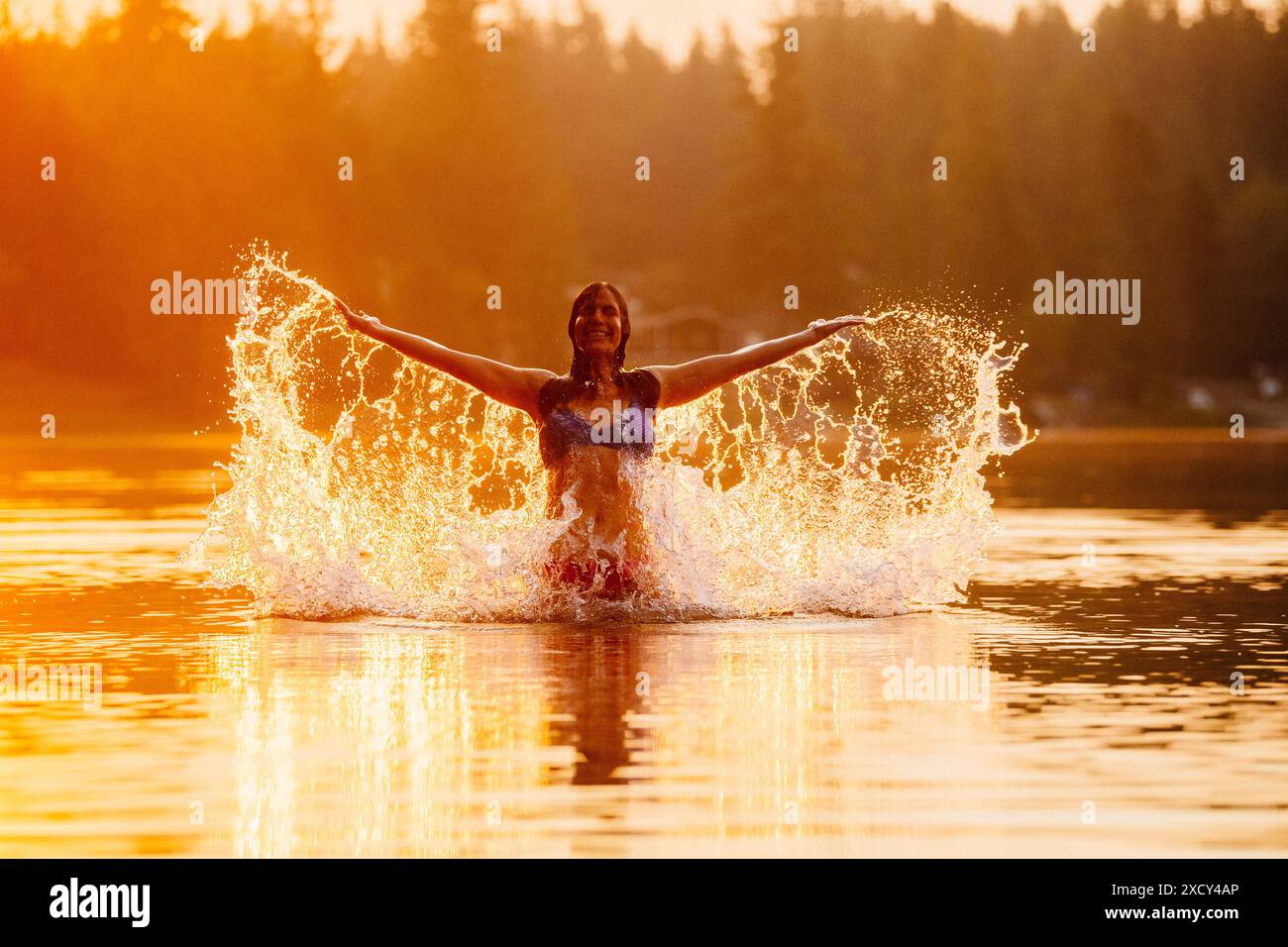 Junge Frau, die in der Abenddämmerung im See planscht Stockfoto