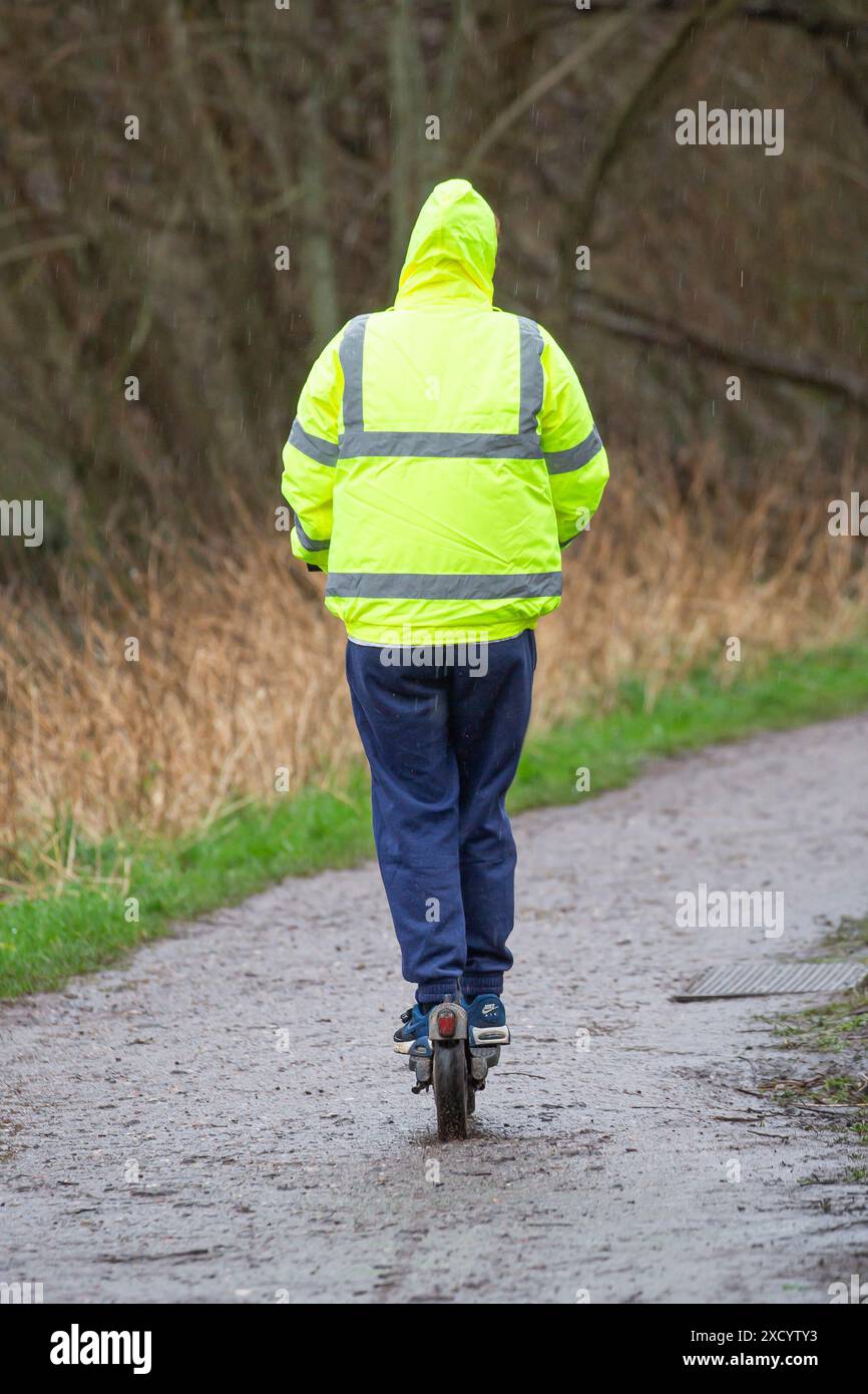 Rückansicht einer Person, die einen Elektroroller mit einer Hi-Viz-Jacke fährt. Stockfoto