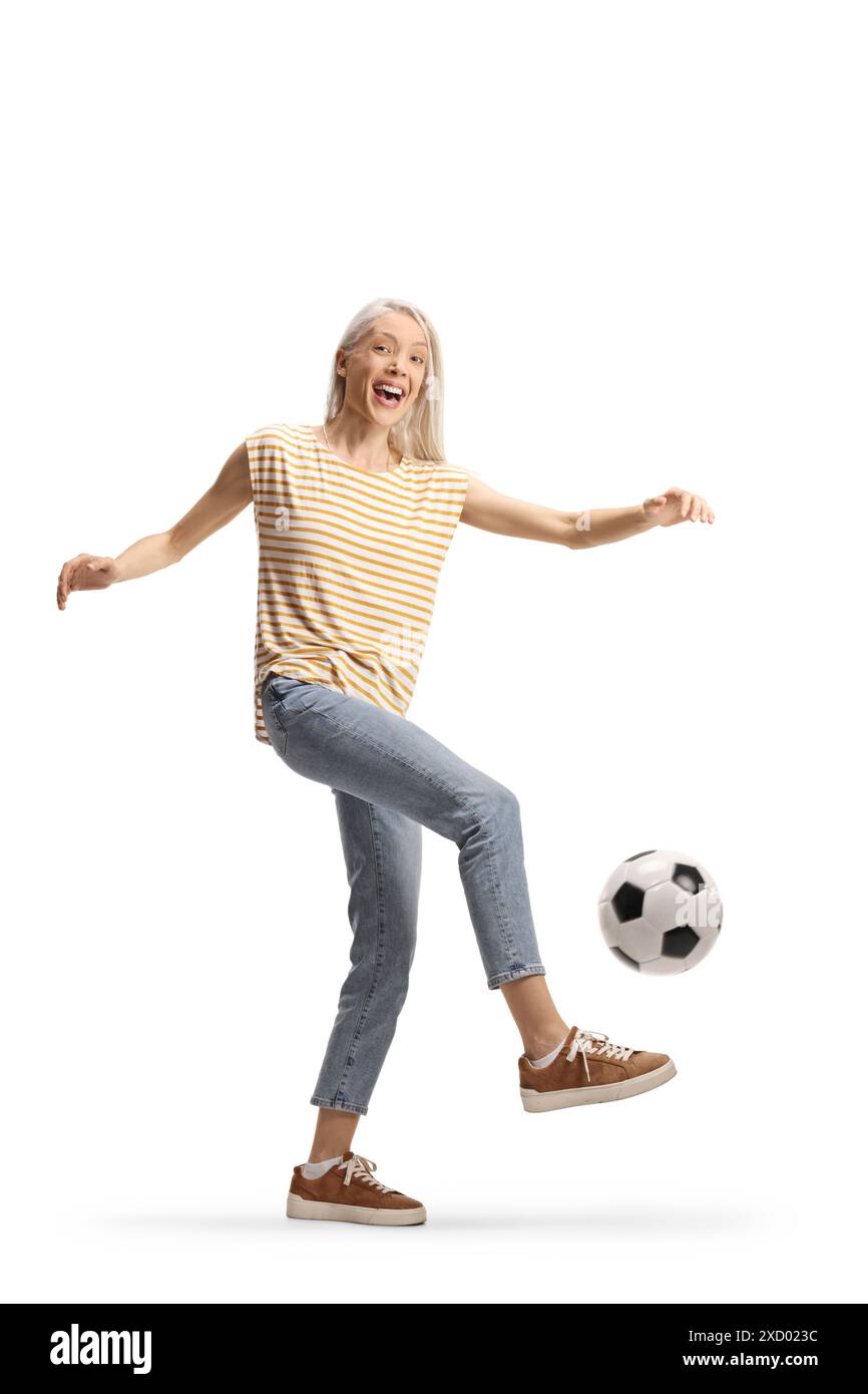 Fröhliche junge Frau, die einen Fußball isoliert auf weißem Hintergrund tritt Stockfoto