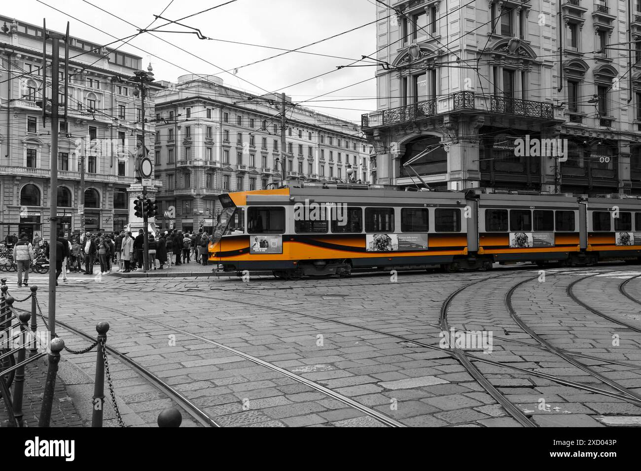 Schwarzweiß mit selektiver Farbe. Orangefarbene Straßenbahn, die an der zentralen Piazza Cordusio, Mailand, Lombardei, Italien vorbeifährt Stockfoto