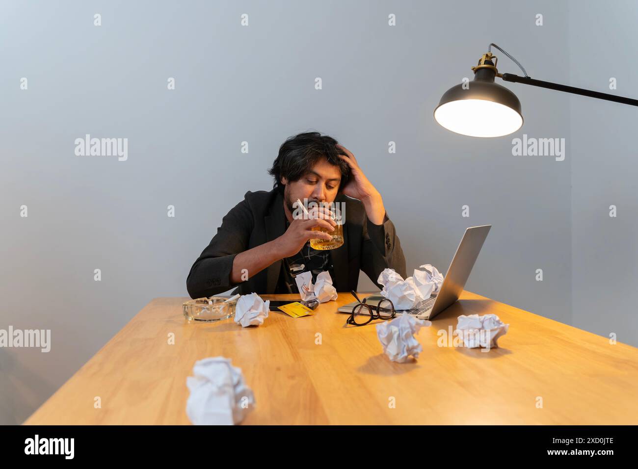Ein Mann sitzt an einem Tisch mit einem Glas Bier und einem Laptop. Er schaut auf den Laptop und ist in einem Zustand der Verwirrung. Der Tisch ist übersichtlich Stockfoto