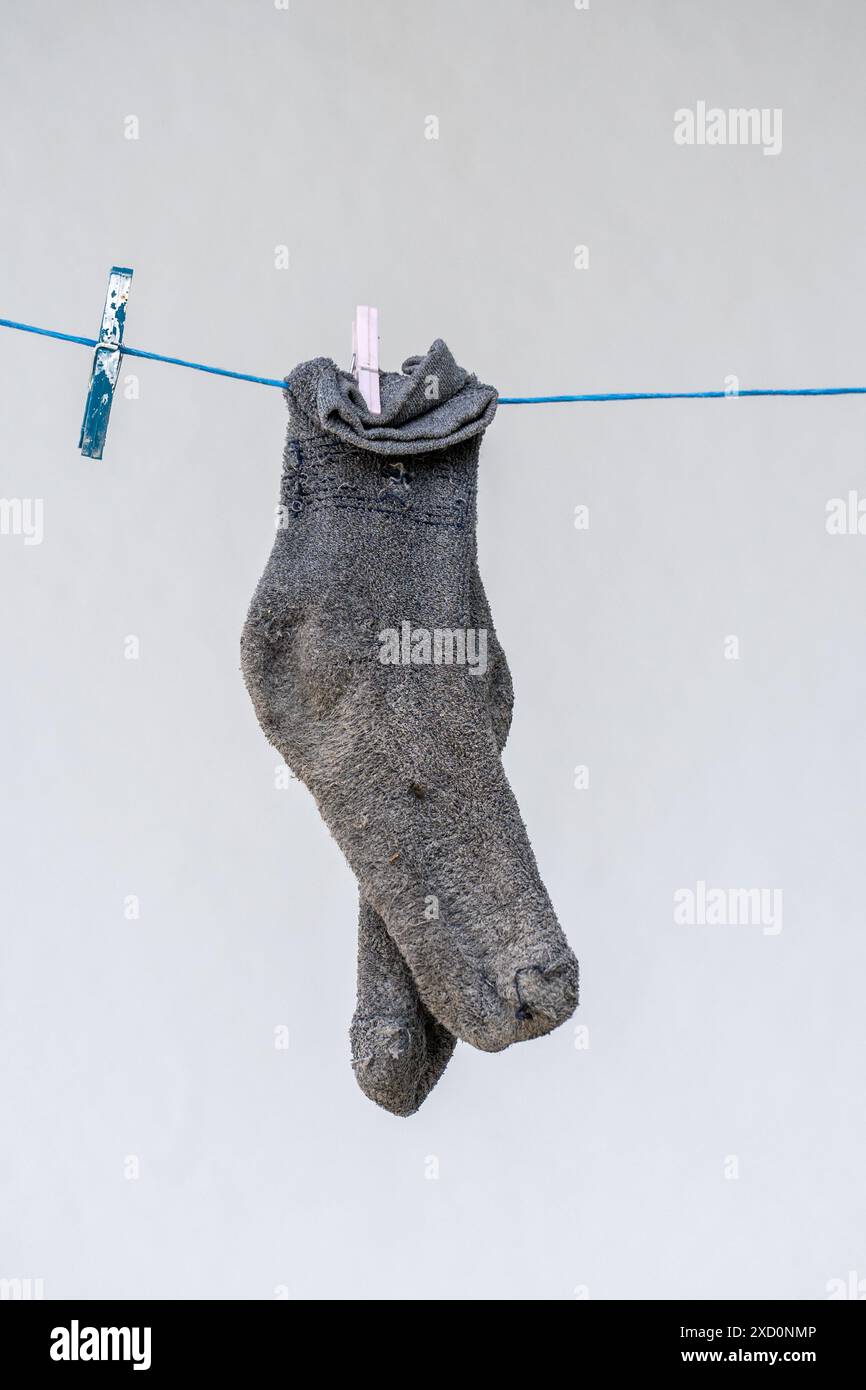 Graue Socken hängen zum Trocknen an einem blauen Seil an einer weißen Wand. Stockfoto