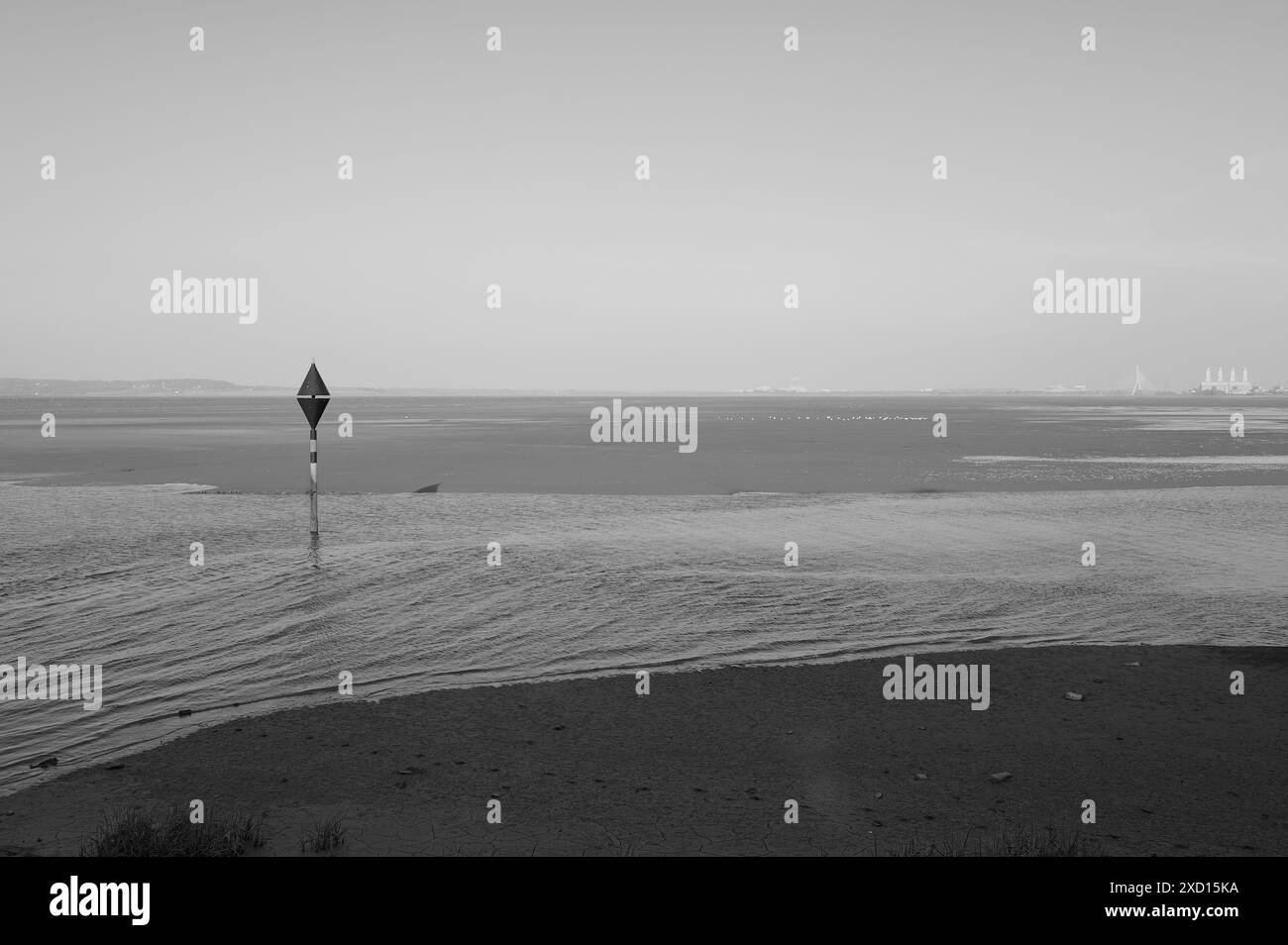 Schwarzweiß-Monoton-Bild der Flussmündung bei Ebbe mit einzelner Gefahrenmarkierung an sonnigem Tag Stockfoto