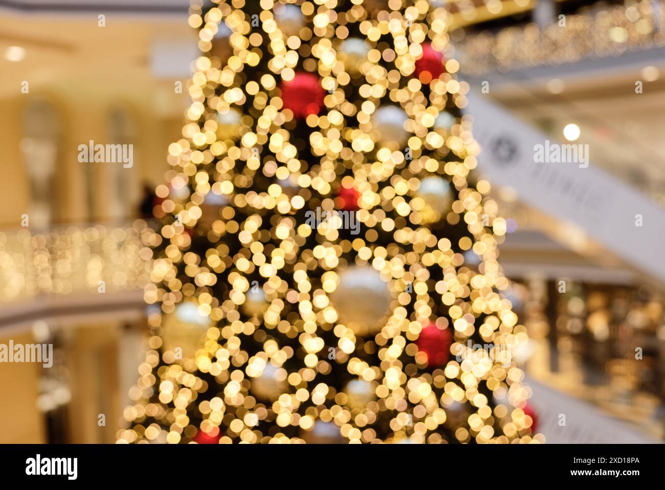Details verschwommener Blick auf einen riesigen Weihnachtsbaum in der zentralen Halle eines großen Einkaufszentrums, mit großen Weihnachtskugeln und vielen LED-Lichtern, Mu Stockfoto