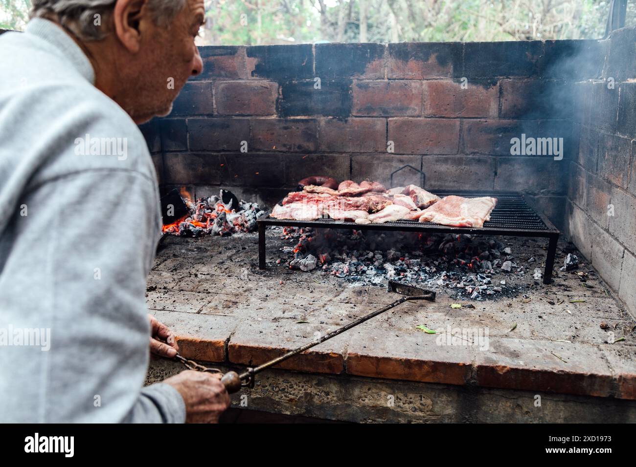 Reifer Mann, der ein Barbecue macht. Argentinisches Fleisch wird auf dem Grill gebraten. Ein traditionelles Barbecue namens Asado in Argentinien. Stockfoto