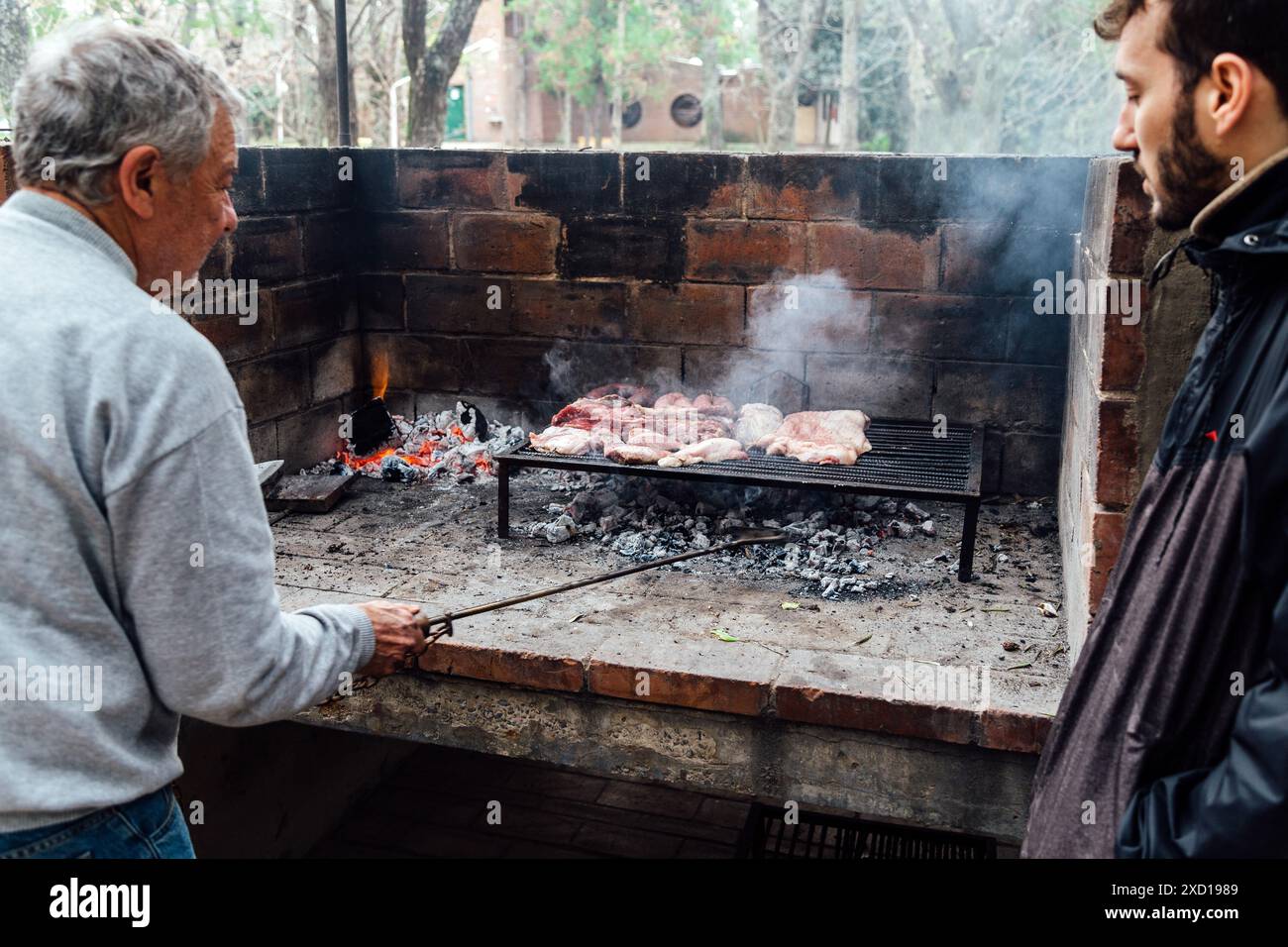 Reifer Mann, der ein Barbecue macht. Argentinisches Fleisch wird auf dem Grill gebraten. Ein traditionelles Barbecue namens Asado in Argentinien. Stockfoto
