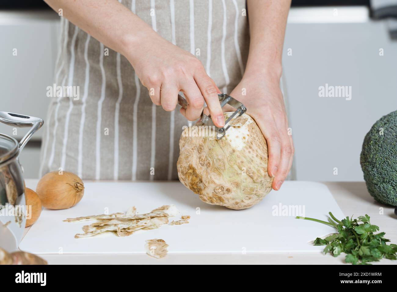 Frau in Schürze, die eine Selleriewurzel oder Sellerie in der Küche schält Stockfoto