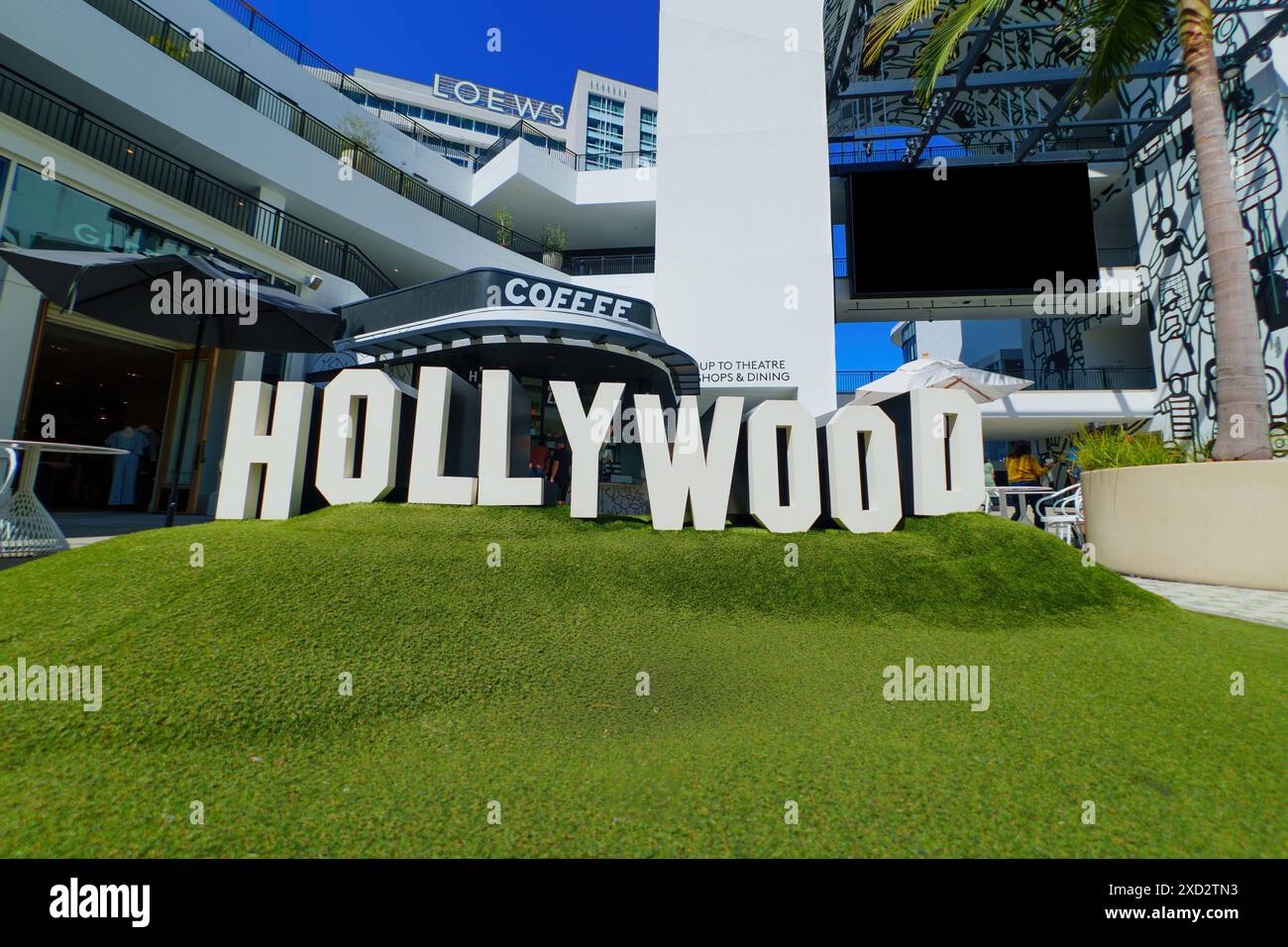 Los Angeles, Kalifornien - 10. April 2024: Nachbildung des berühmten Hollywood-Schildes in der FIGat7th Mall, umgeben von grünem Rasen, Geschäften und Plakatwänden. Stockfoto