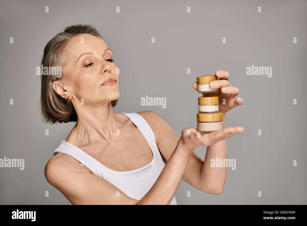 Eine reife Frau in bequemer Kleidung hält anmutig eine Flasche Creme. Stockfoto