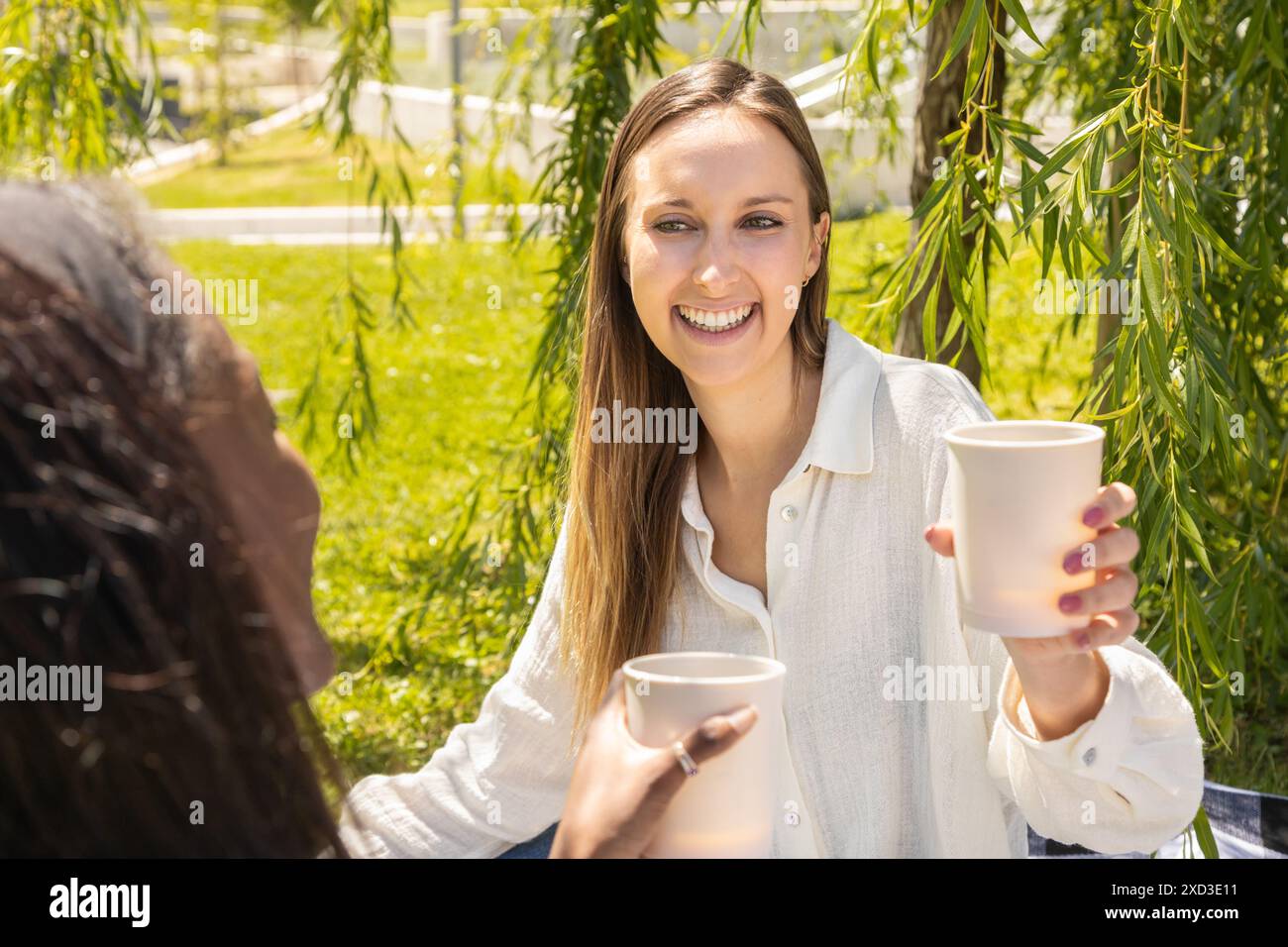 In einer üppigen Umgebung im Freien führen zwei professionelle multirassische Frauen eine freundliche Unterhaltung bei einem Kaffee, was ein Beispiel für eine entspannte Arbeitsumgebung ist Stockfoto