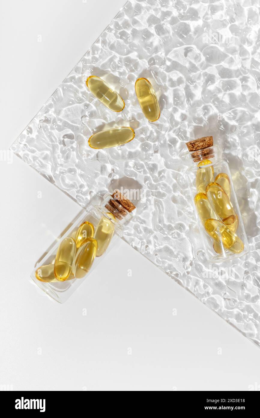 Omega 3 Kapseln auf einer strukturierten Glasplatte mit lichtreflektierenden Mustern, die den goldenen Farbton und die transparente Schale der Pillen hervorheben, EM Stockfoto