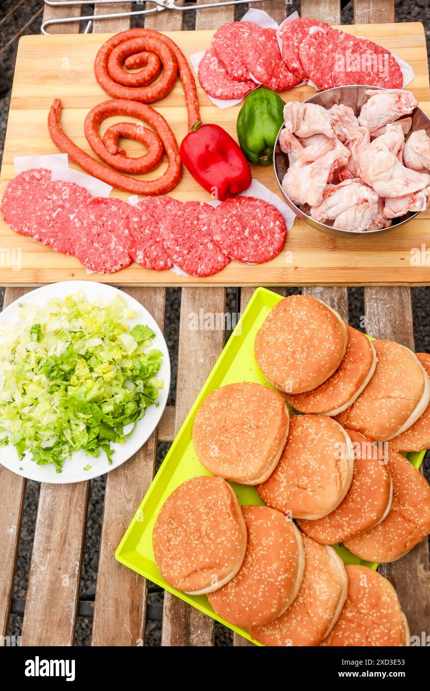 Blick von oben auf eine lebhafte Auswahl an rohen Grillgerichten, darunter Würstchen, Burger Patties, Hähnchenstücke, rote und grüne Paprika und Cho Stockfoto