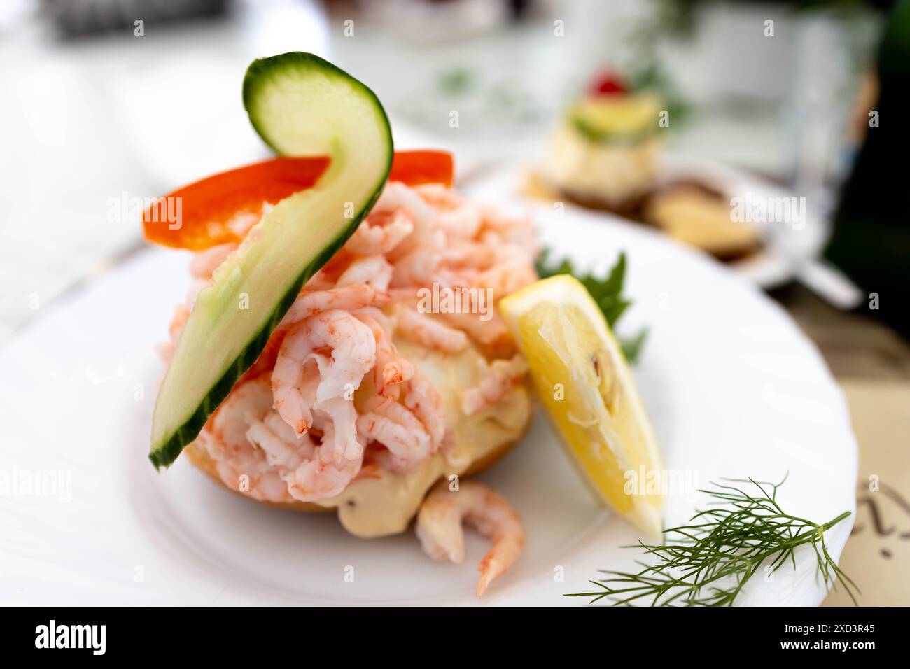 Ein köstliches Garnelensalat-Sandwich garniert mit Gurke, Paprika und Zitrone, serviert auf einem weißen Teller. Stockfoto