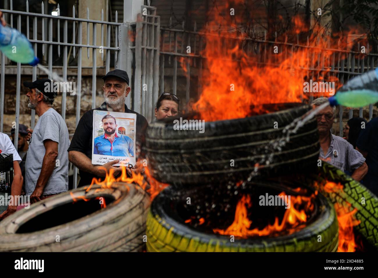 Beirut, Libanon. 20. Juni 2024, Beirut, Beirut, Libanon: Vater von Ahmad al-Kaadan, der bei der massiven Explosion des Hafens am 5. August 2020 ums Leben kam, trägt sein Bild hinter brennenden Reifen im Justizpalast von BeirutÃ¢â‚¬â„¢während eines Protestes von Familien der Opfer der Explosion. Weniger als zwei Monate bis zum 4. Jahrestag der Explosion, bei der mehr als 200 Menschen ums Leben kamen, ist fast alles unbekannt Ã¢â‚¬ von der Person, die die Verbringung angeordnet hat, bis hin zu den wiederholten Warnungen der Beamten vor der Gefahr. Quelle: ZUMA Press, Inc./Alamy Live News Stockfoto